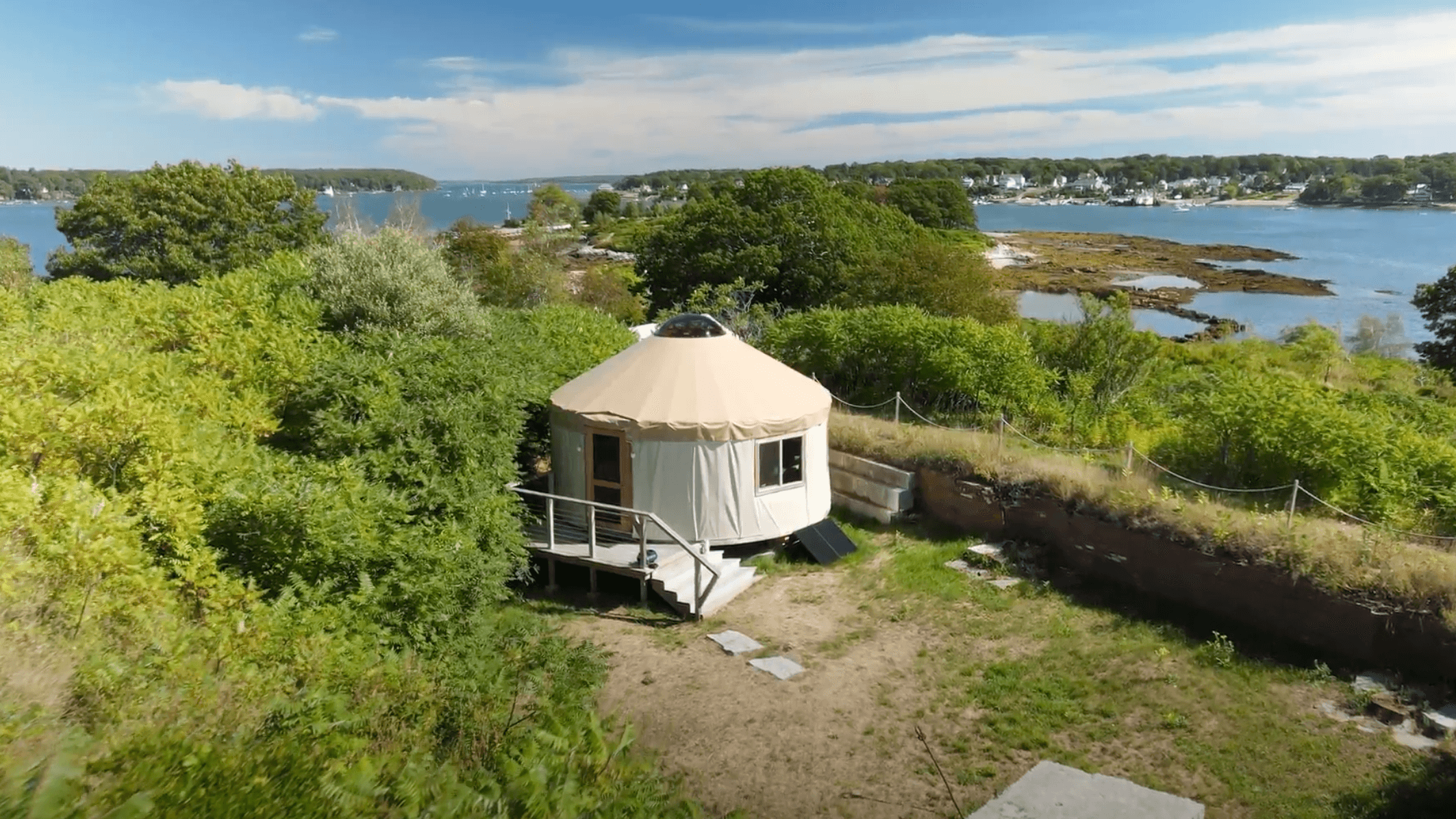 A yurt surrounded by greenery with a scenic view of a river and distant coastline.