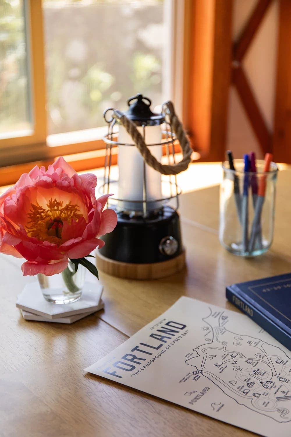 A vibrant pink flower in a vase beside a lantern and stationery on a wooden table.