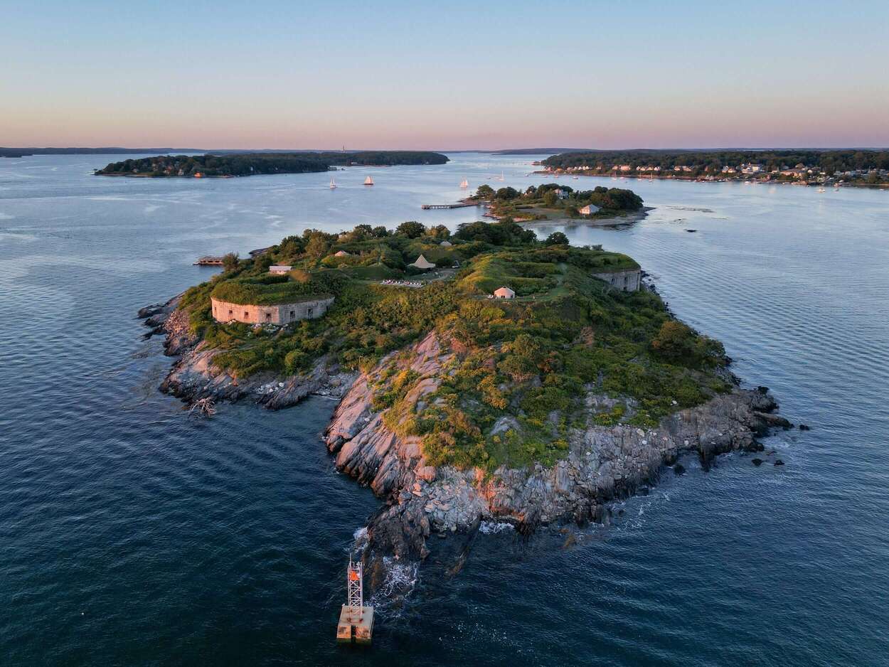 Aerial view of a small, lush island featuring a historic stone fort surrounded by water at sunset.