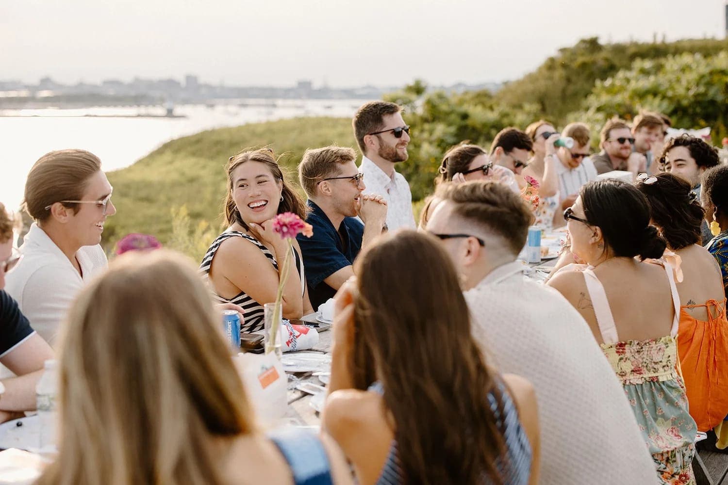 A lively outdoor gathering with friends enjoying a meal by the water.