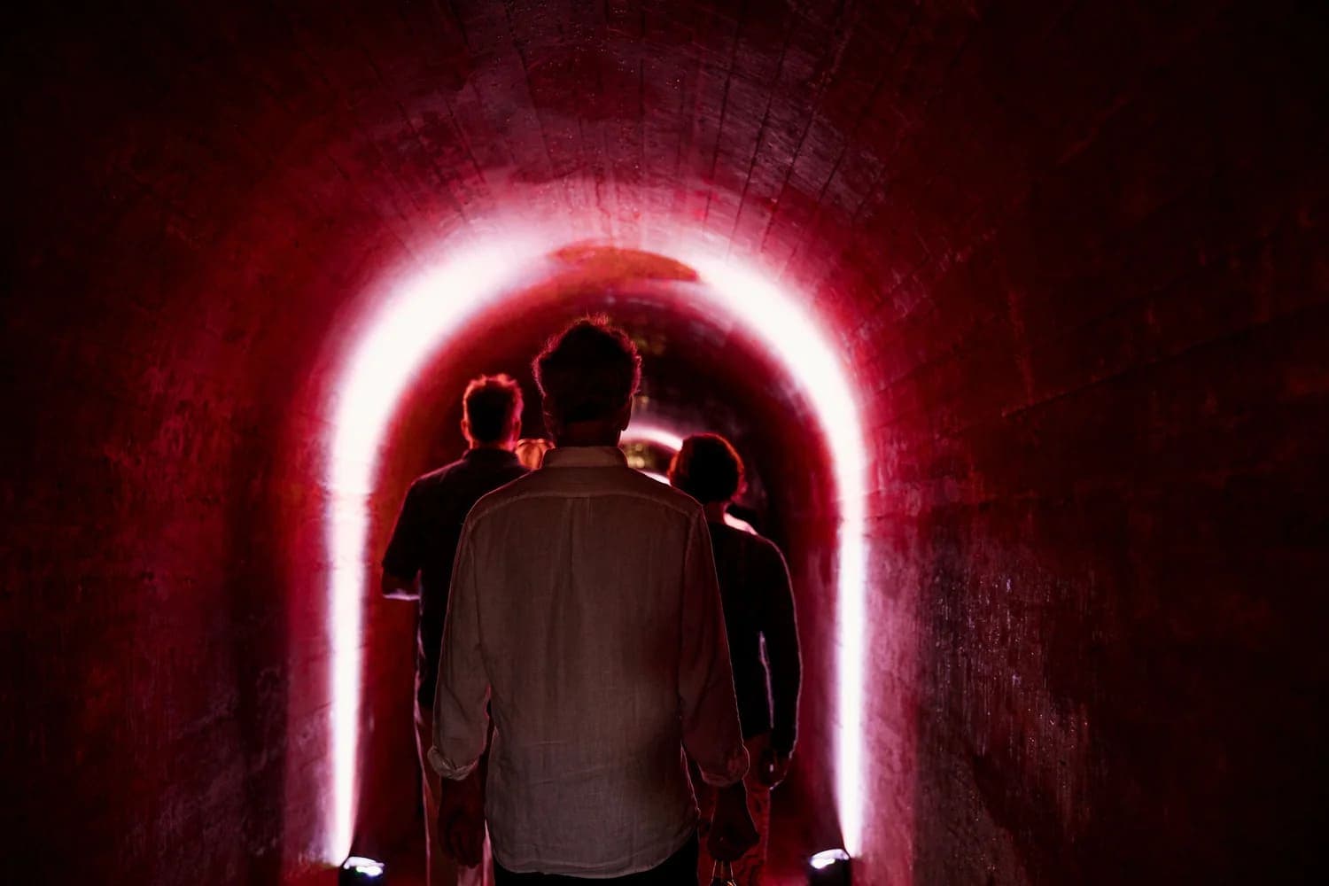 Three figures walking through a dimly lit, red-tinted tunnel.