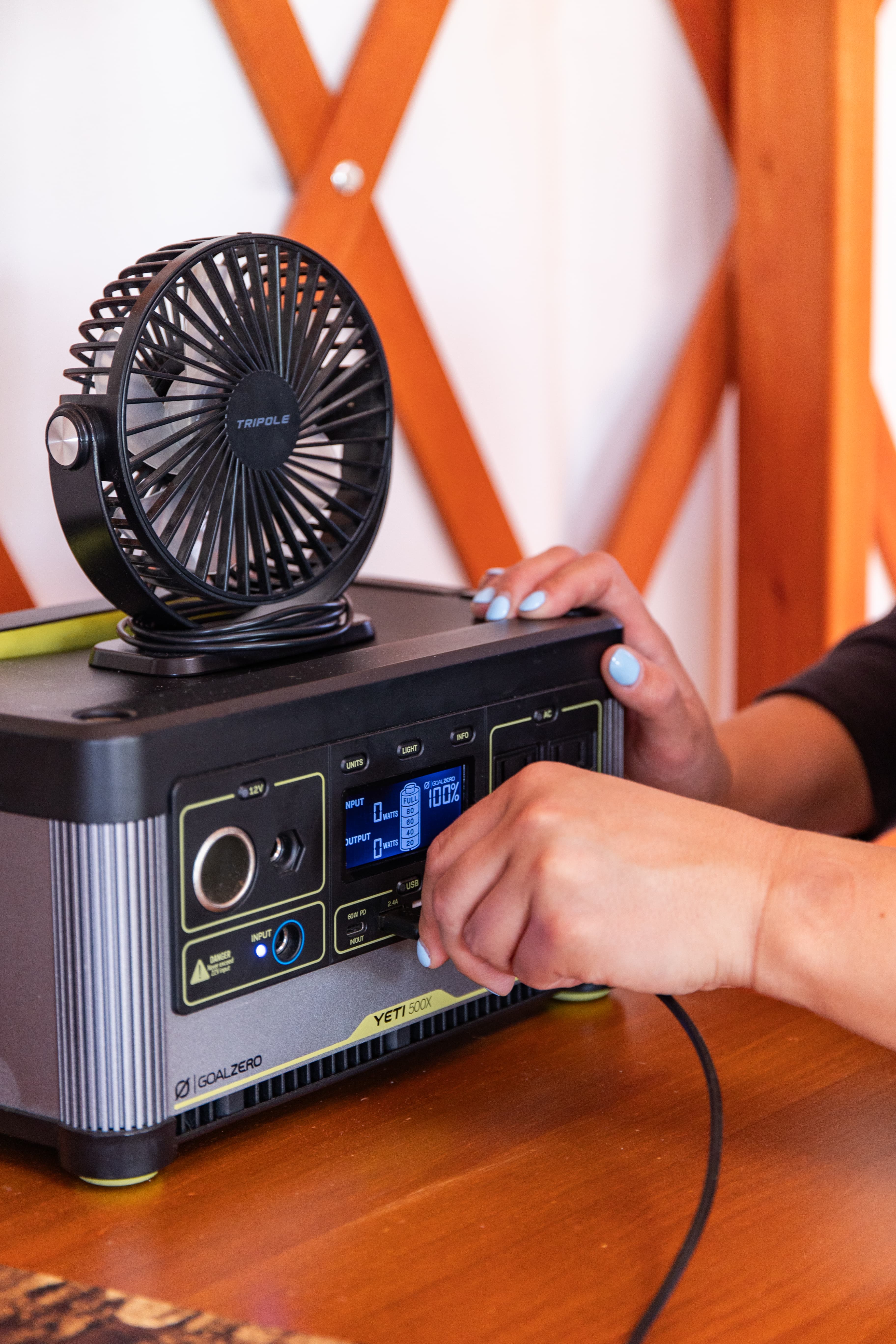 A person adjusts the controls on a portable power station with a small fan on top, set against a wooden background.