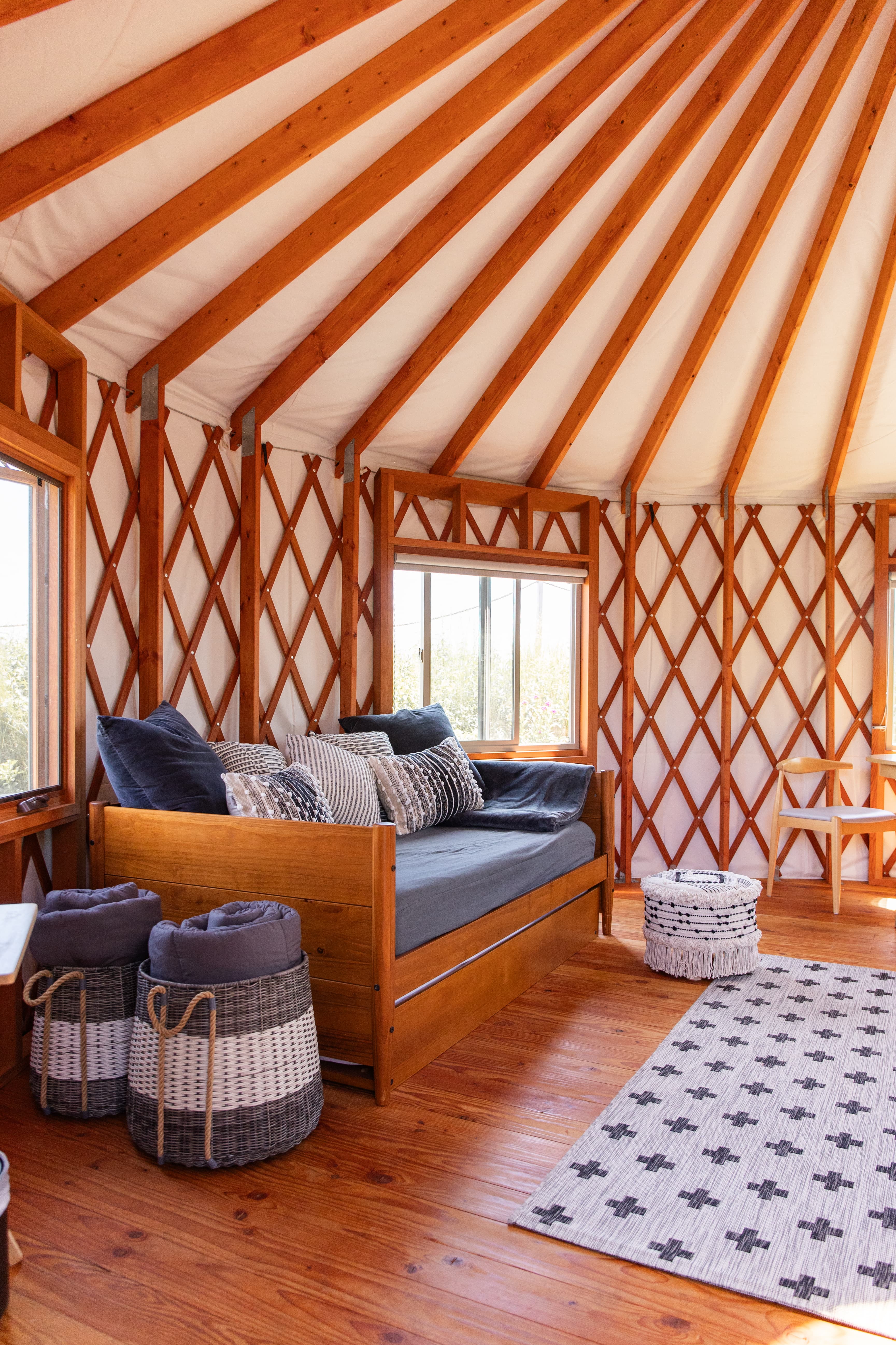 Cozy interior of a yurt featuring a daybed, decorative pillows, and woven storage baskets.