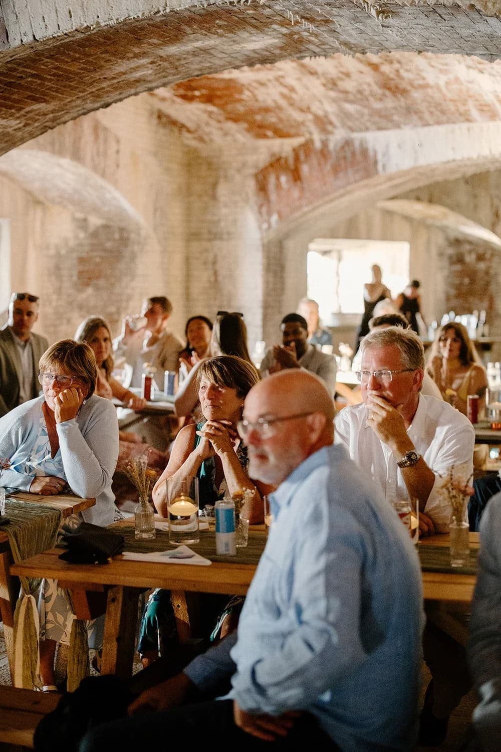 A diverse group of people attentively listening in a rustic, softly lit venue.