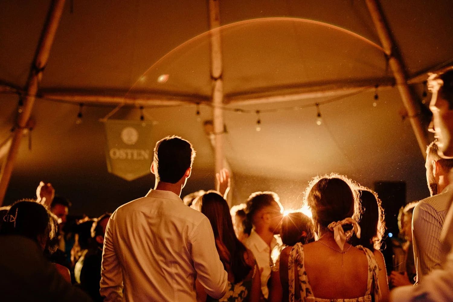 A crowd of people dancing under soft lighting inside a tent.