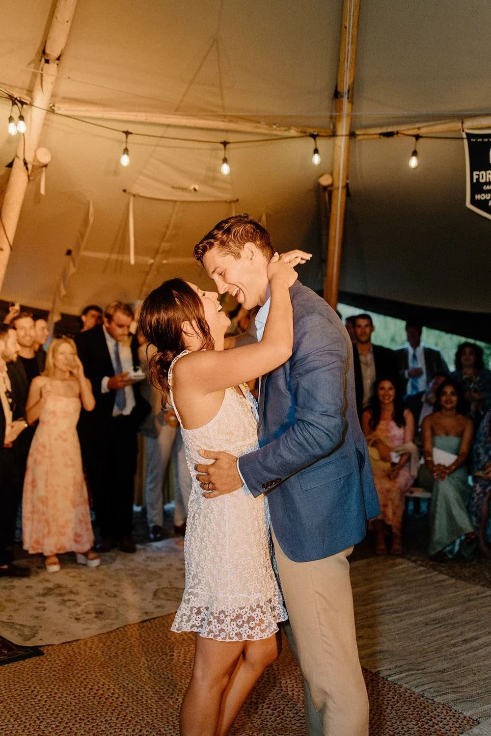 A couple dances closely in a tent, surrounded by guests enjoying a festive atmosphere.