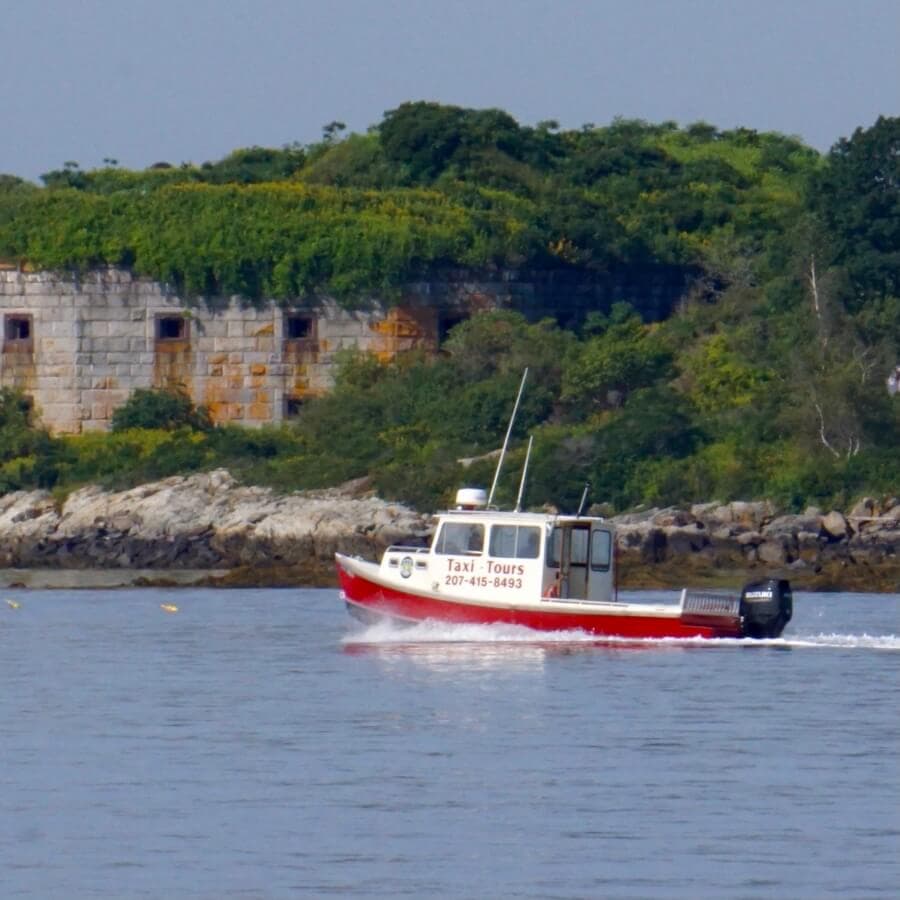 A red and white taxi boat navigates the calm waters near a lush, green coastal backdrop.