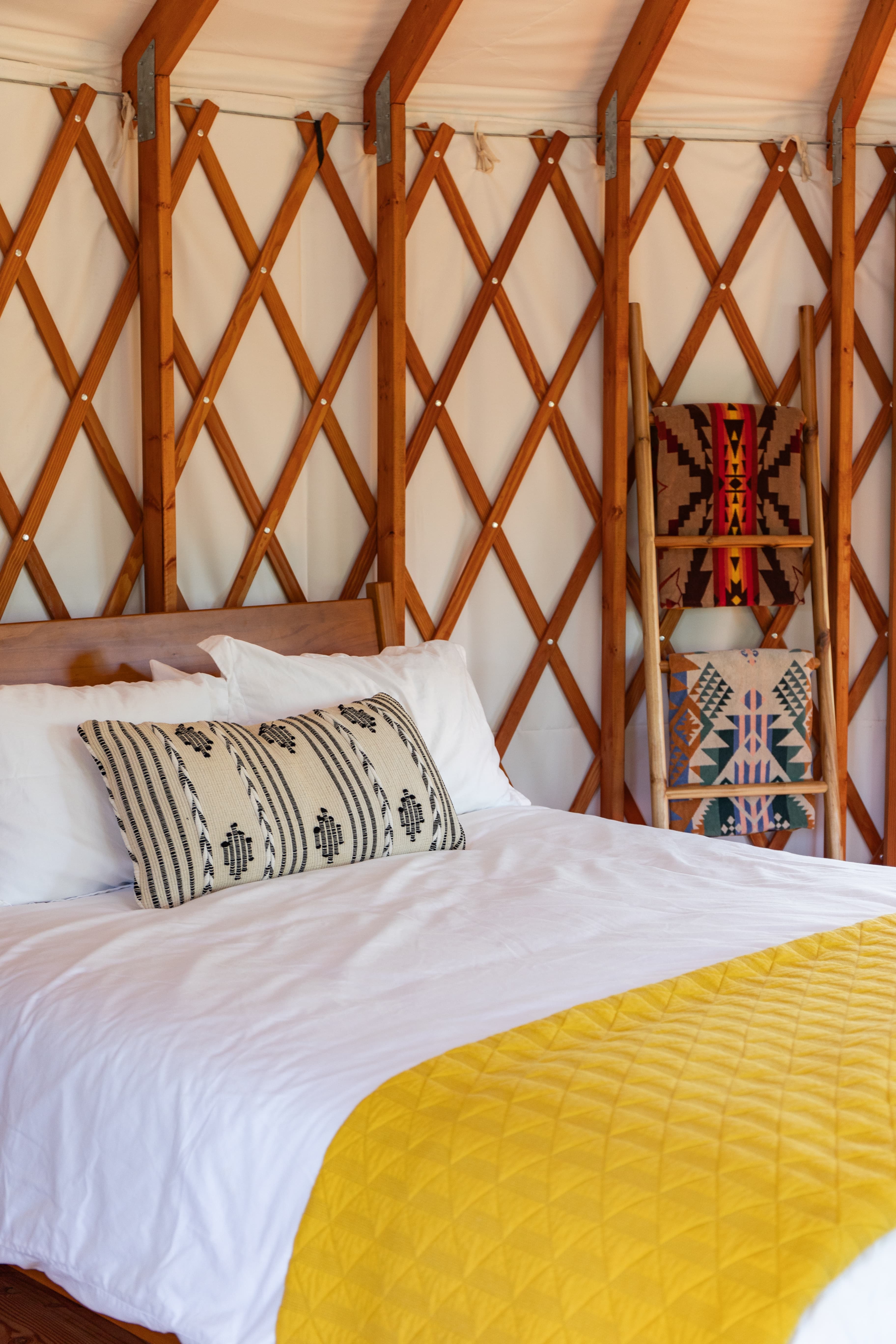 A cozy bed with a yellow quilt and patterned pillows inside a yurt.