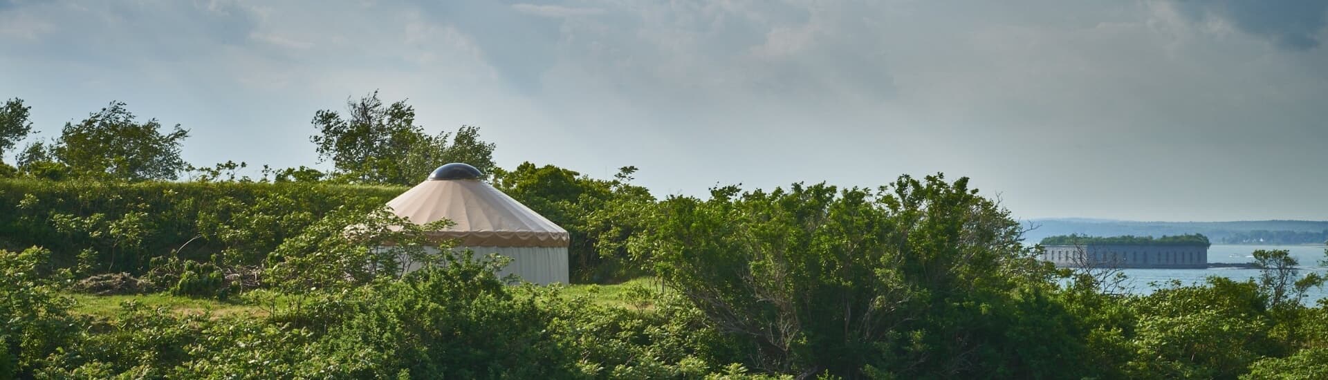 A yurt nestled among lush greenery with a coastal view in the background.