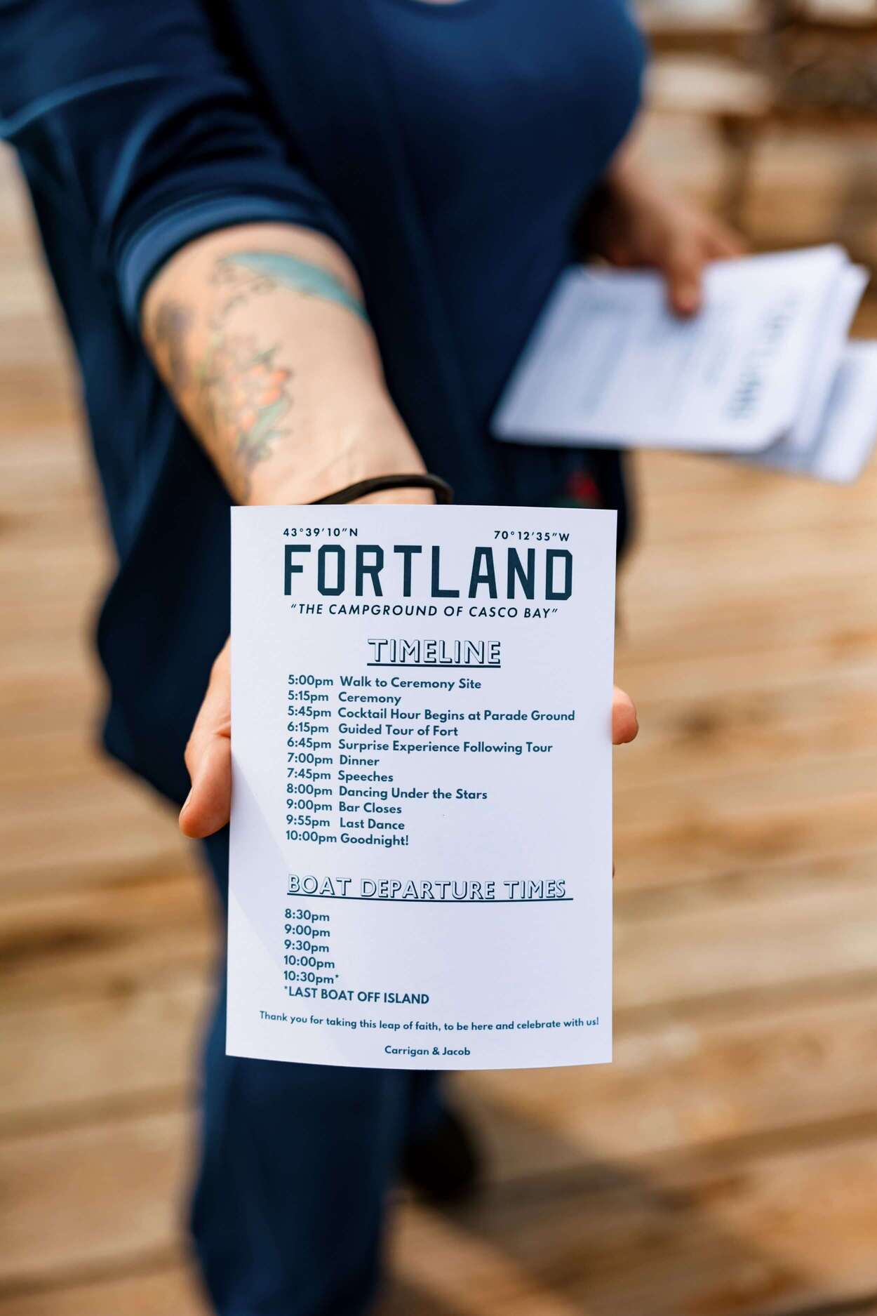 A person holds a printed timeline and schedule for an event titled "Fortland: The Campground of Casco Bay."