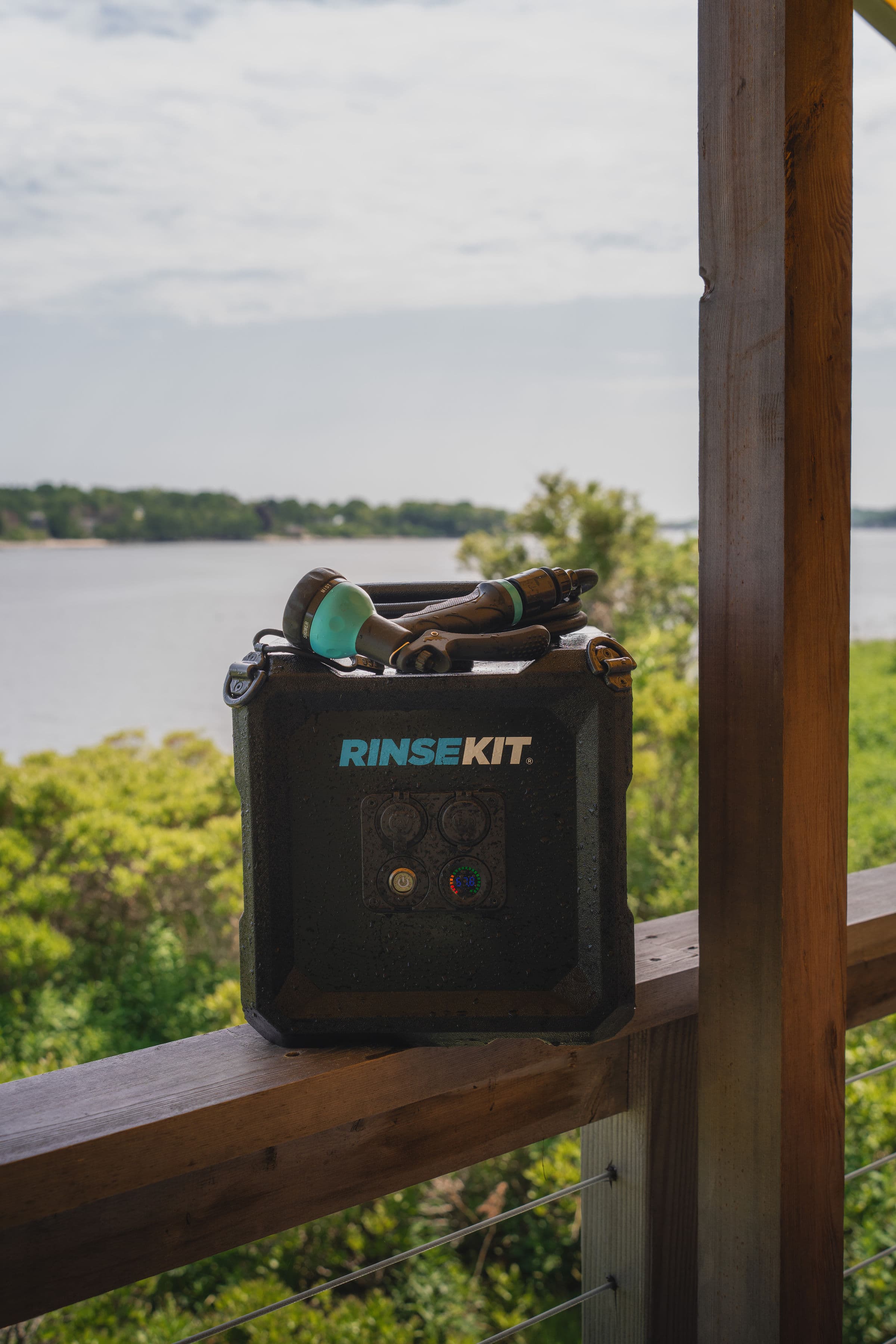 A portable RinseKit with a hose is placed on a wooden railing overlooking a body of water.