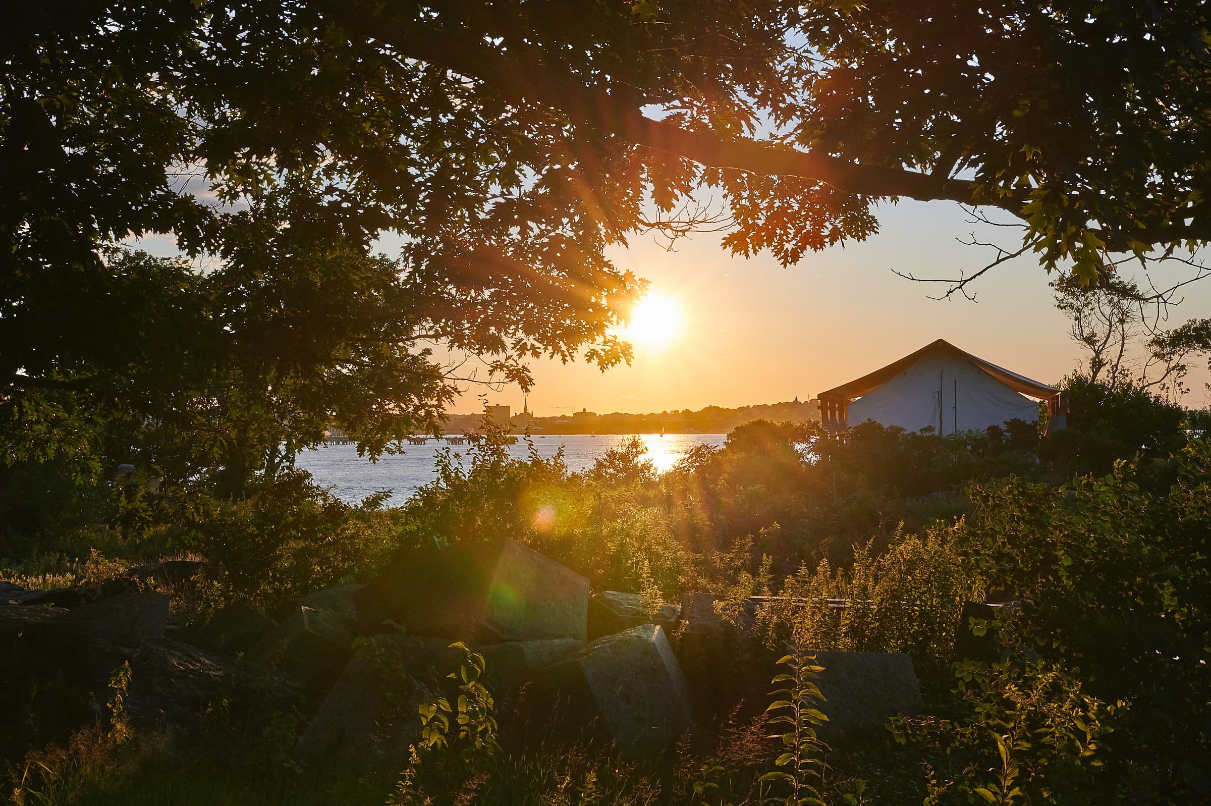 Sunset over a river framed by trees and a building in the background.