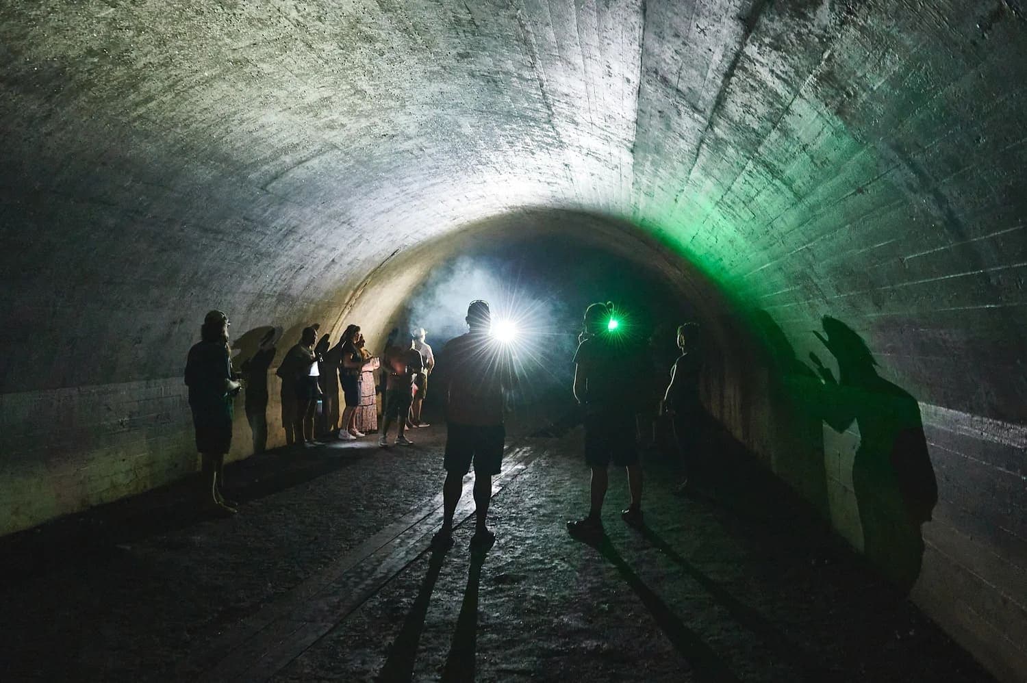 A group of people stands in a dark tunnel illuminated by green and white lights.