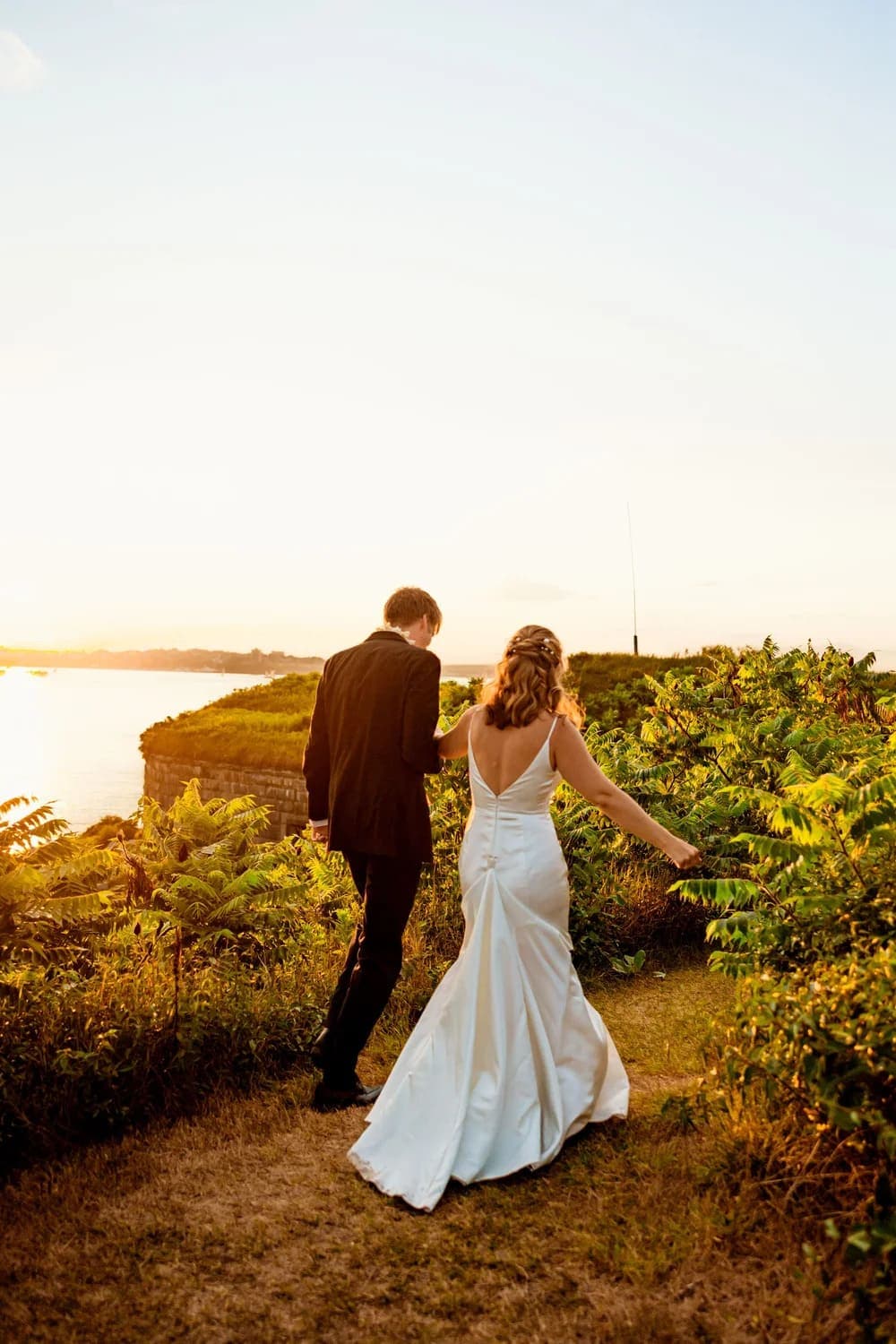 A couple walks hand-in-hand along a scenic path at sunset, surrounded by greenery.