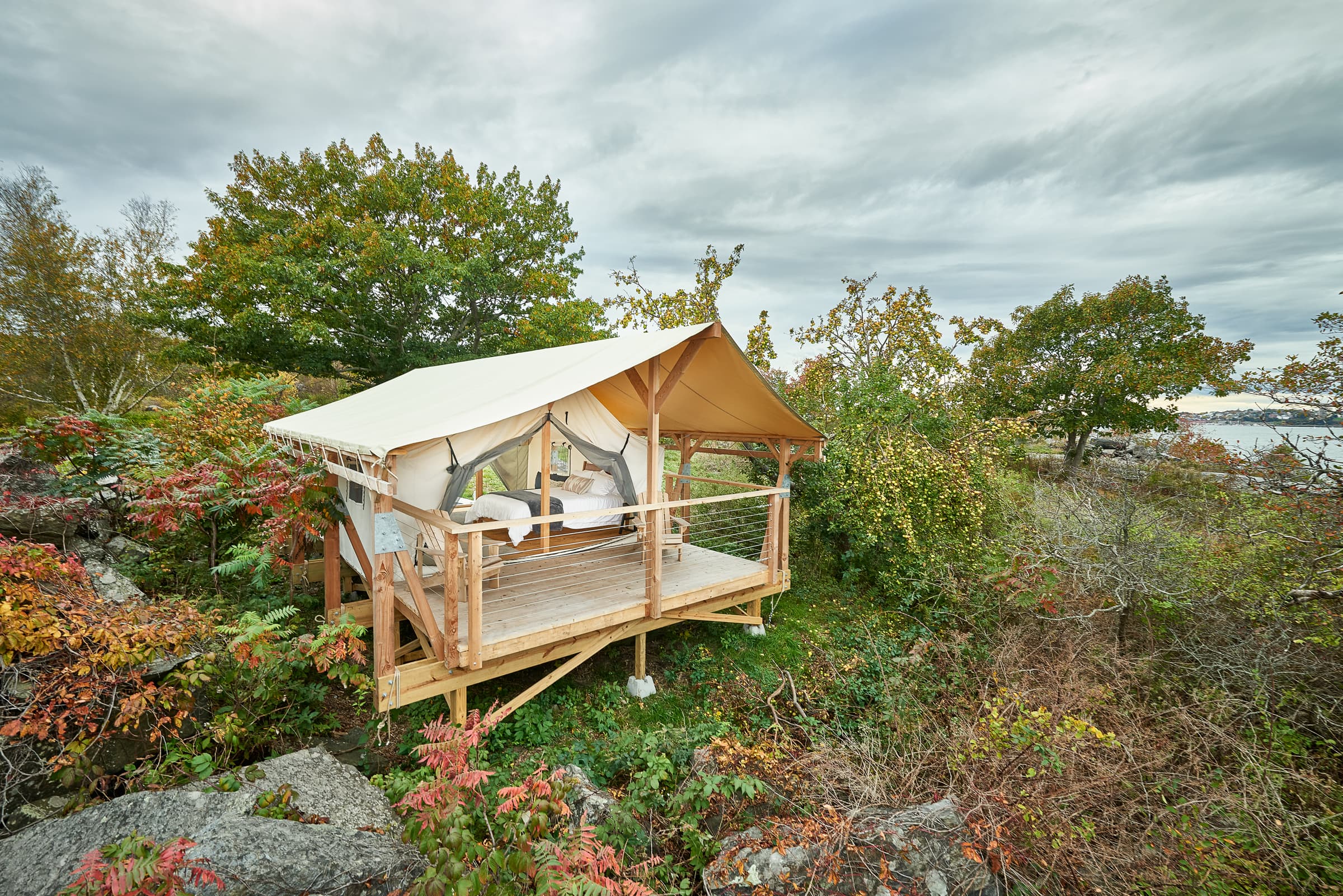 A cozy tent on a wooden deck surrounded by lush greenery and autumn foliage.