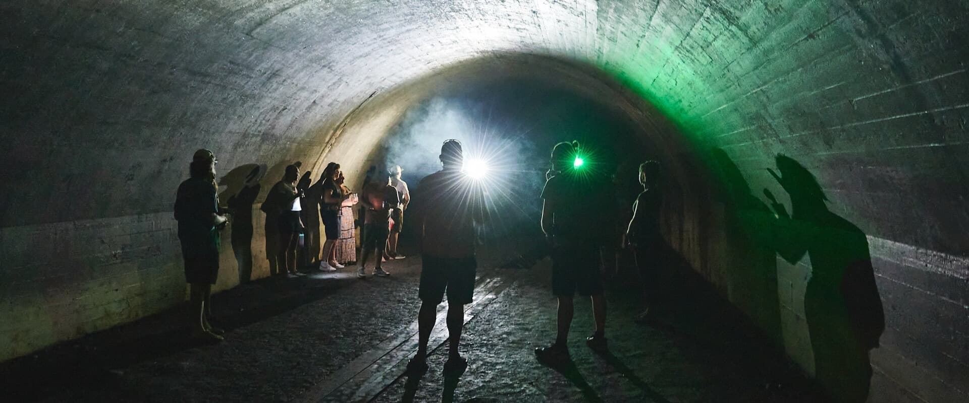 A group of people stands in a dimly lit tunnel, illuminated by various lights and shadows.
