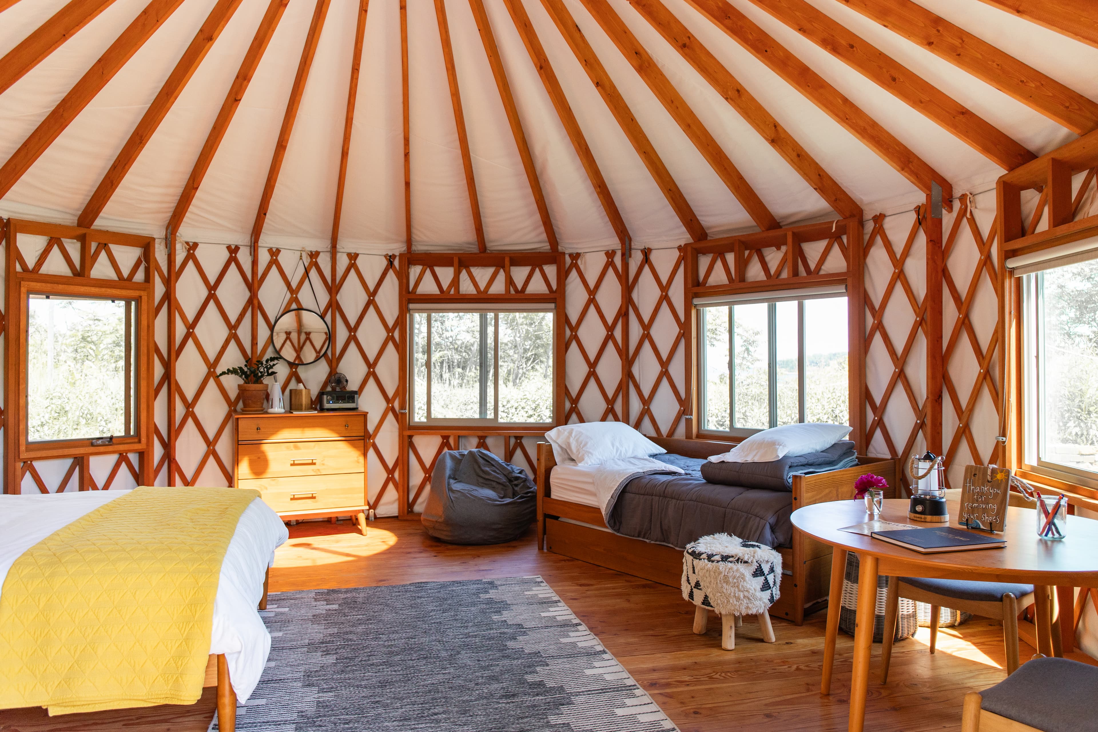 Interior of a yurt featuring wooden beams, a rug, two beds, and a dining table with chairs.