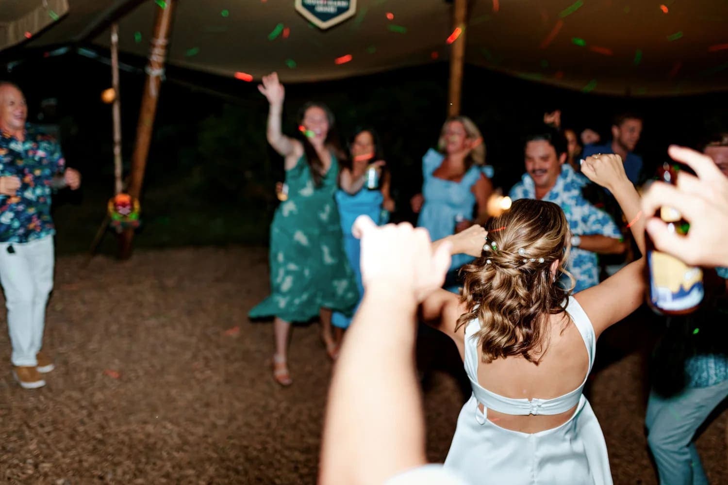 A group of people dance joyfully at a nighttime celebration under a tent.