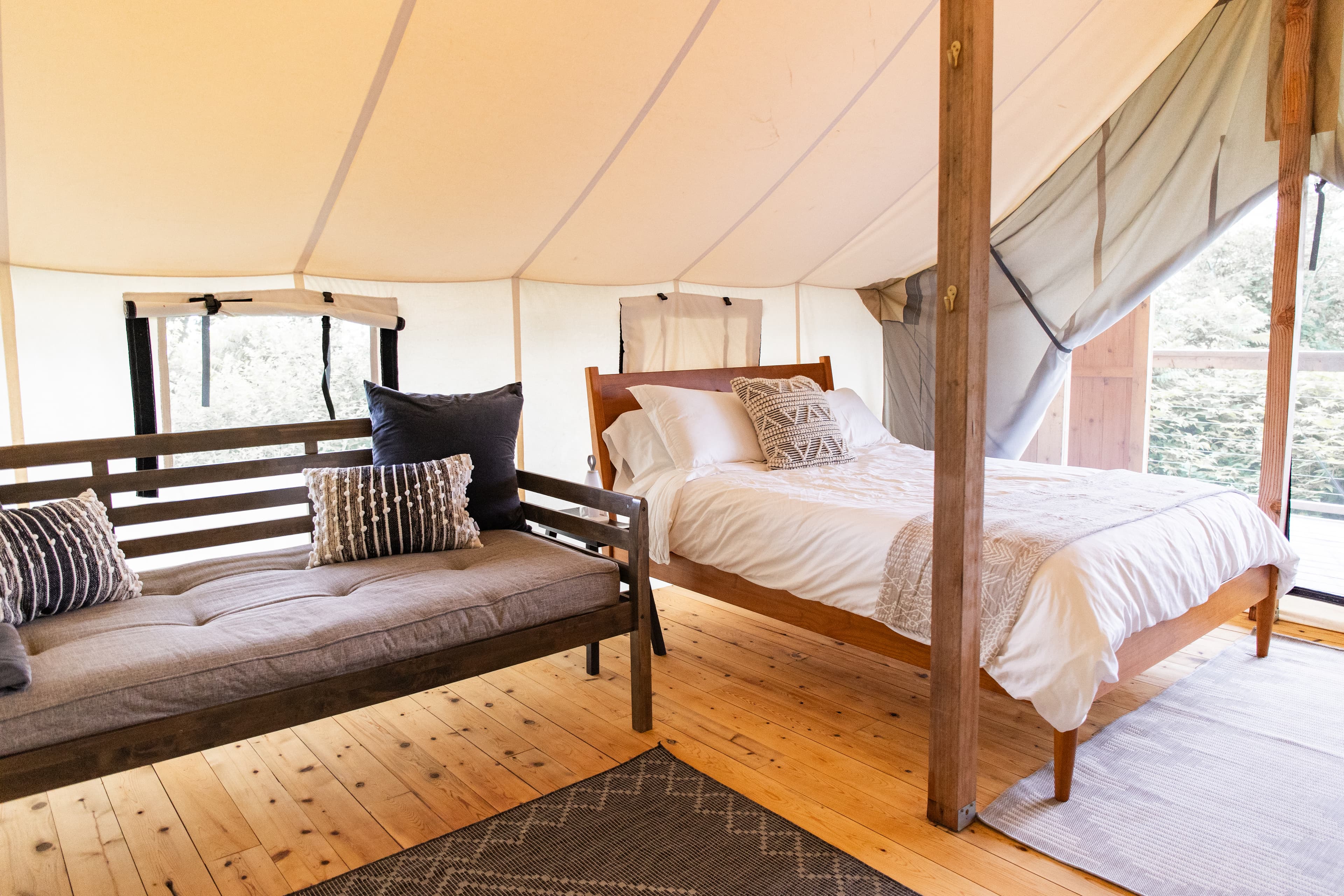 A cozy tent interior featuring a bed, a daybed, and wooden flooring.