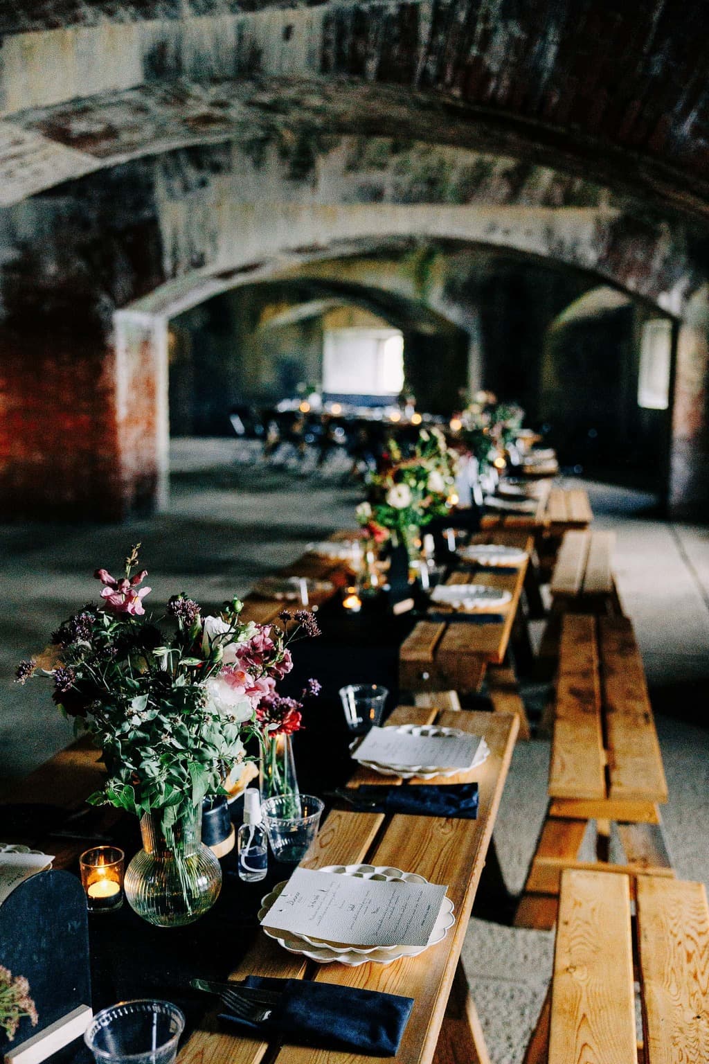 A beautifully arranged long dining table with floral centerpieces and elegant place settings in a rustic, arched space.