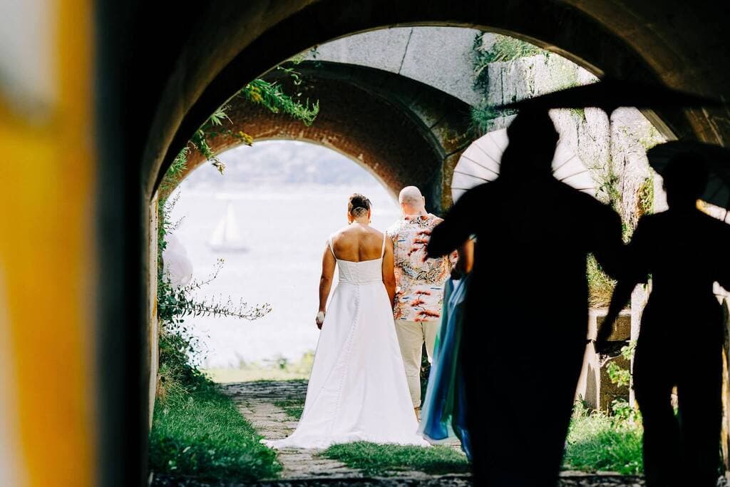 A bride in a white dress stands with her back to the camera, framed by an archway, while a figure in dark clothing approaches.