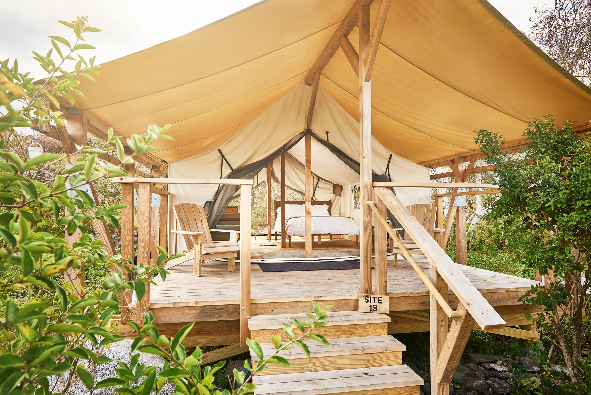A cozy, elevated glamping tent with wooden decking and chairs, surrounded by greenery.