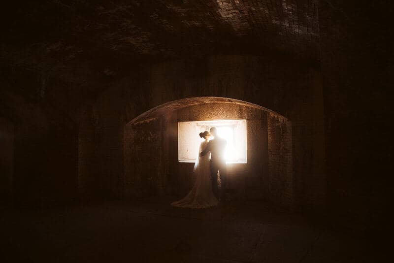 Silhouette of a couple embracing in a dimly lit, arched space with a glowing window.