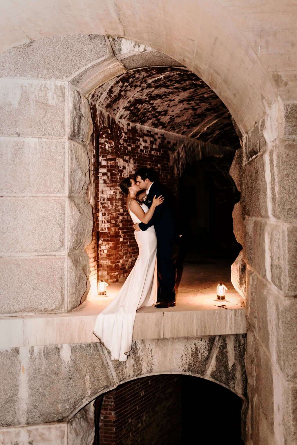 A couple embraces and kisses in a dimly lit archway.