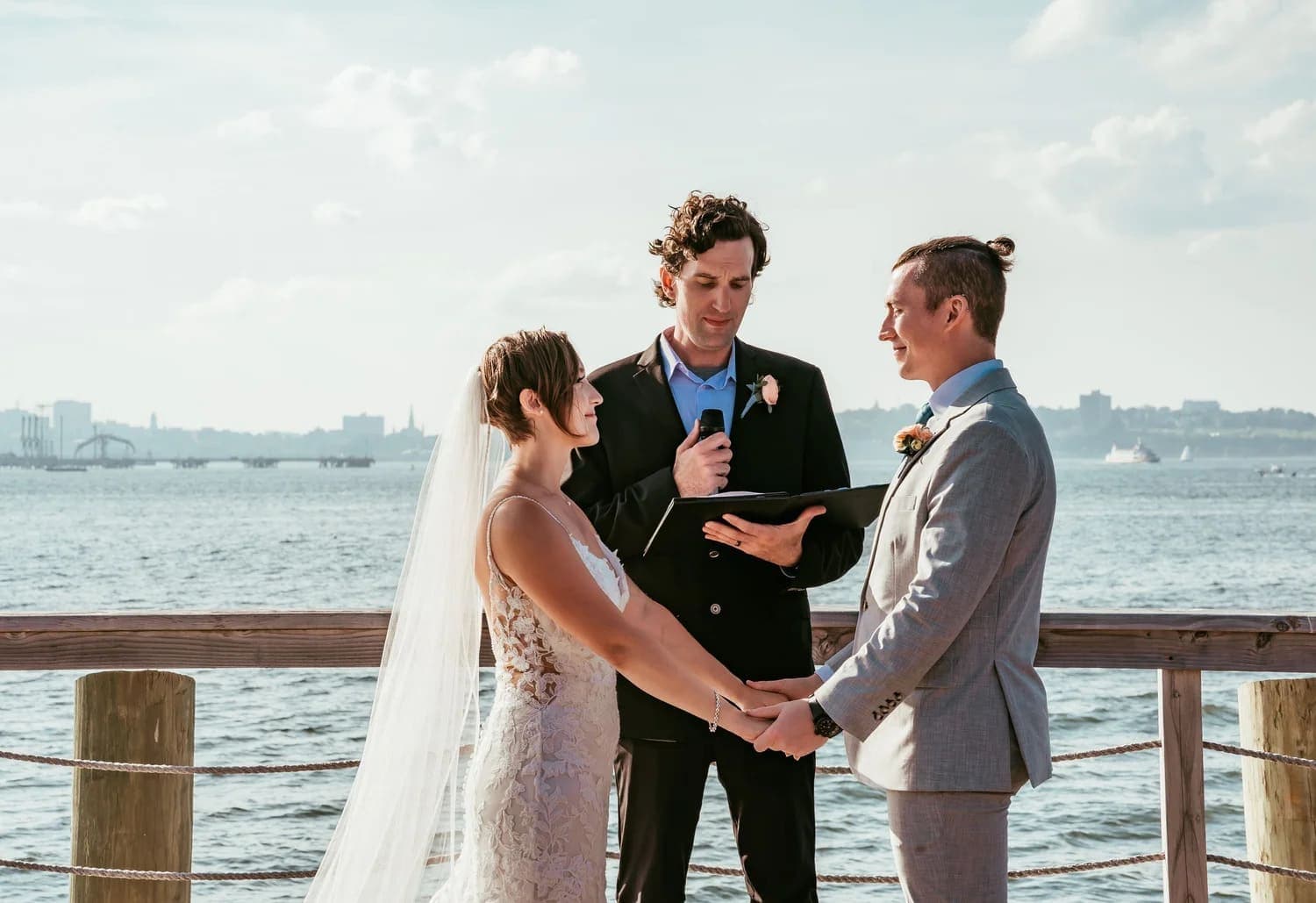 A couple exchanges vows during an outdoor wedding ceremony by the water.