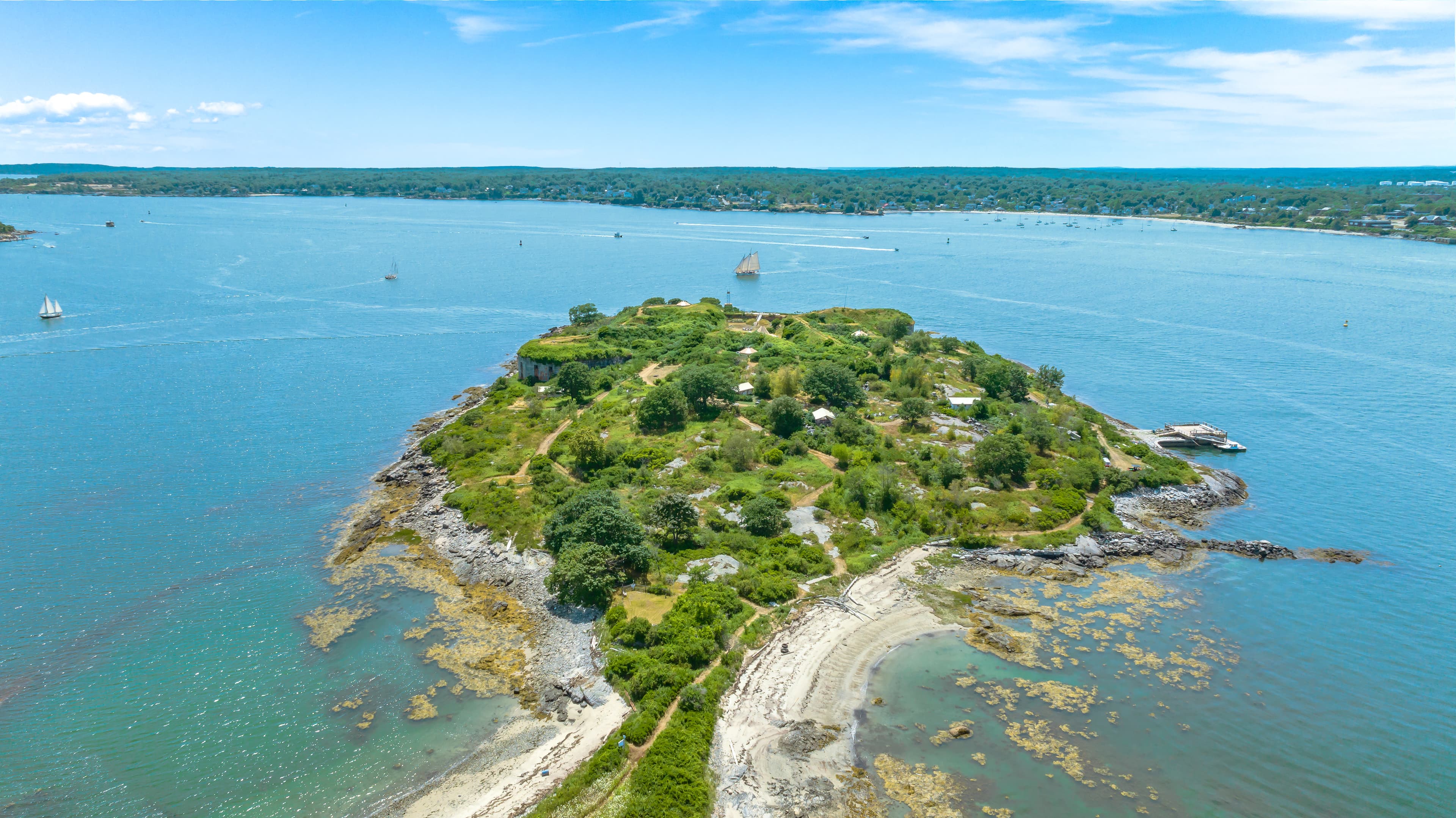 Aerial view of a lush, green island surrounded by blue water and sailboats.