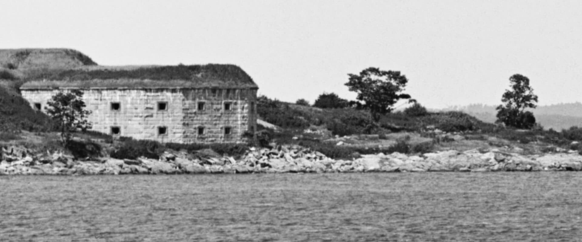 Black and white image of a weathered stone building on a rocky shoreline.