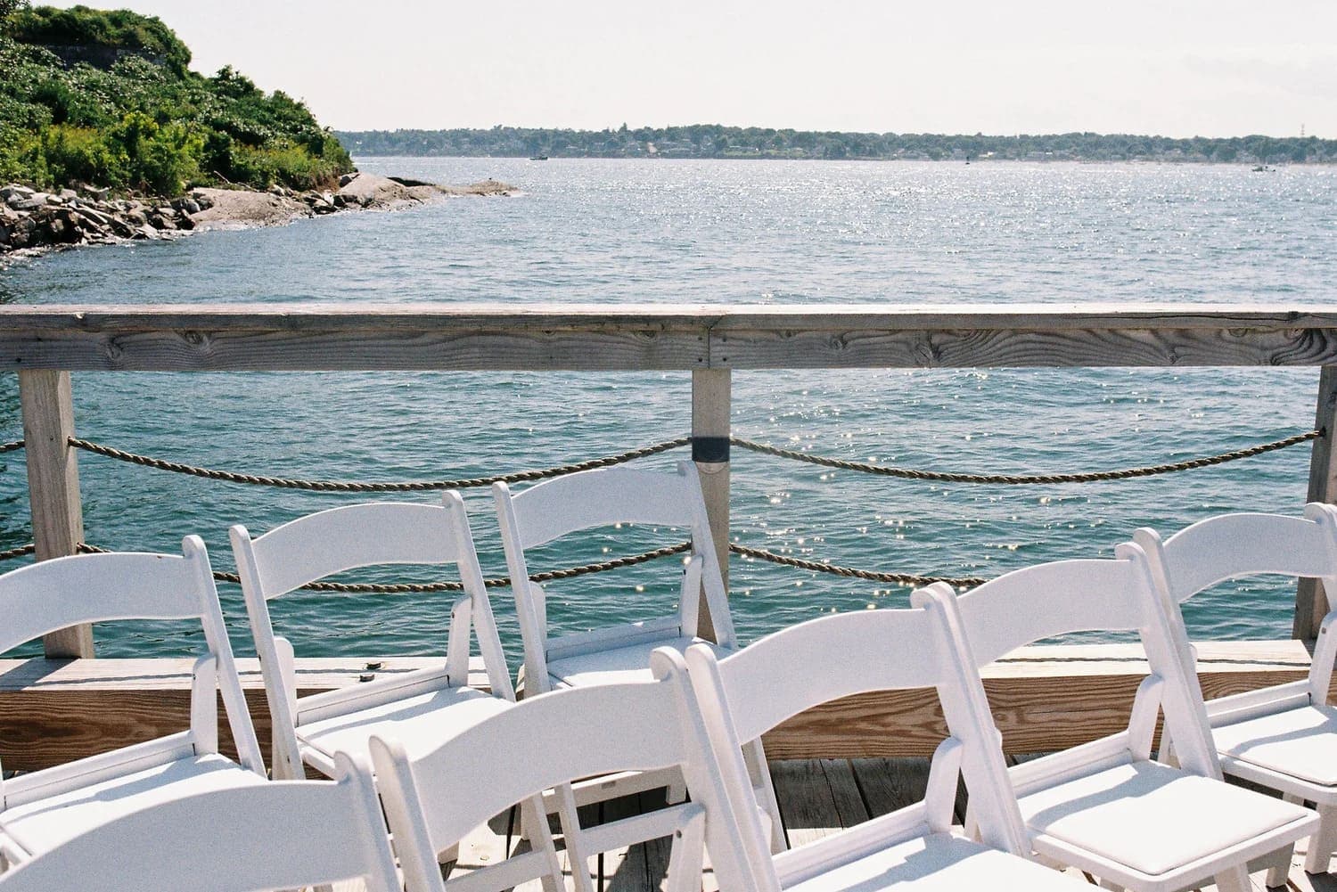 White chairs set up along a wooden deck overlooking a tranquil body of water.