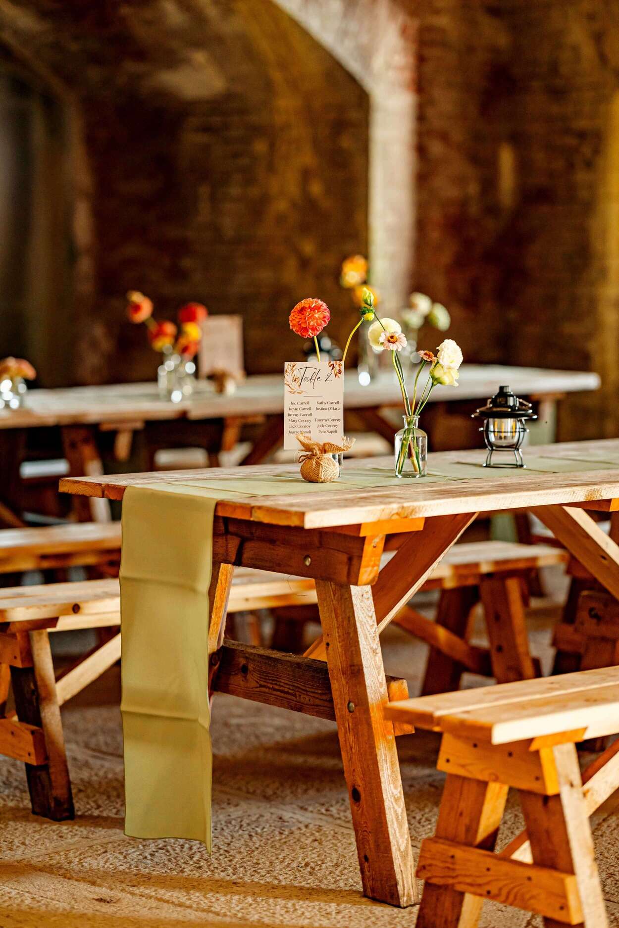 Wooden tables set with small flower arrangements and a menu in a rustic venue.
