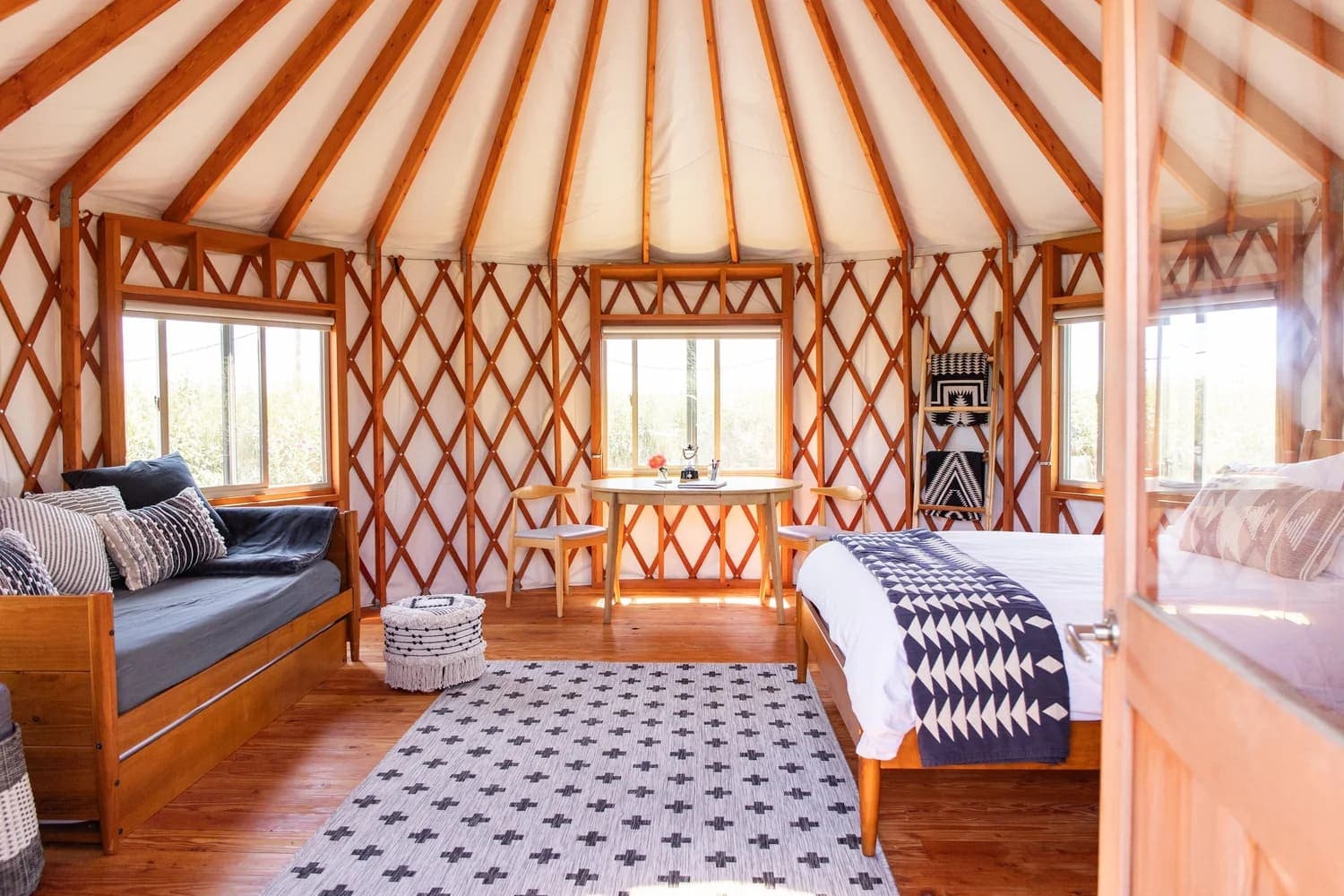 Interior of a cozy yurt featuring a bed, seating area, and large windows.