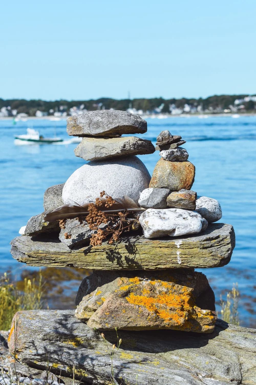 A stacked arrangement of stones with a backdrop of calm water and distant shoreline.