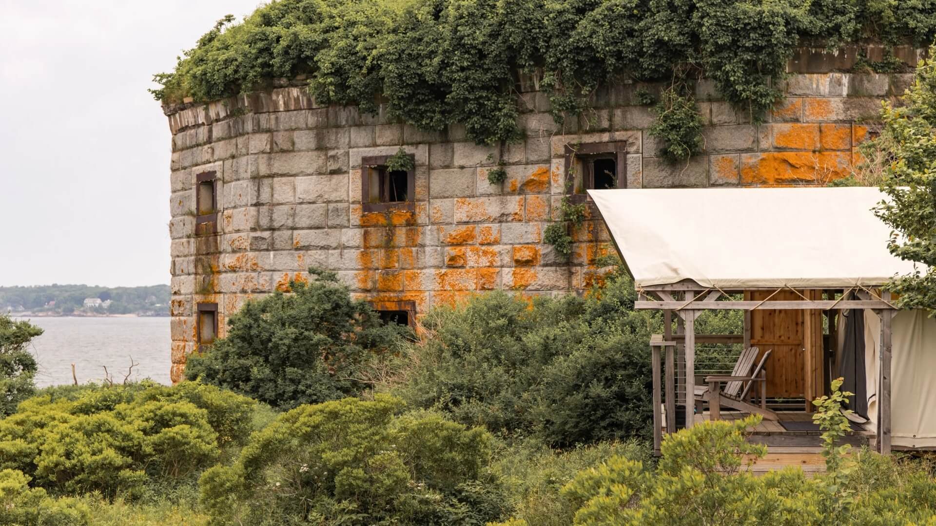An overgrown stone fort with a nearby wooden structure and lush vegetation.