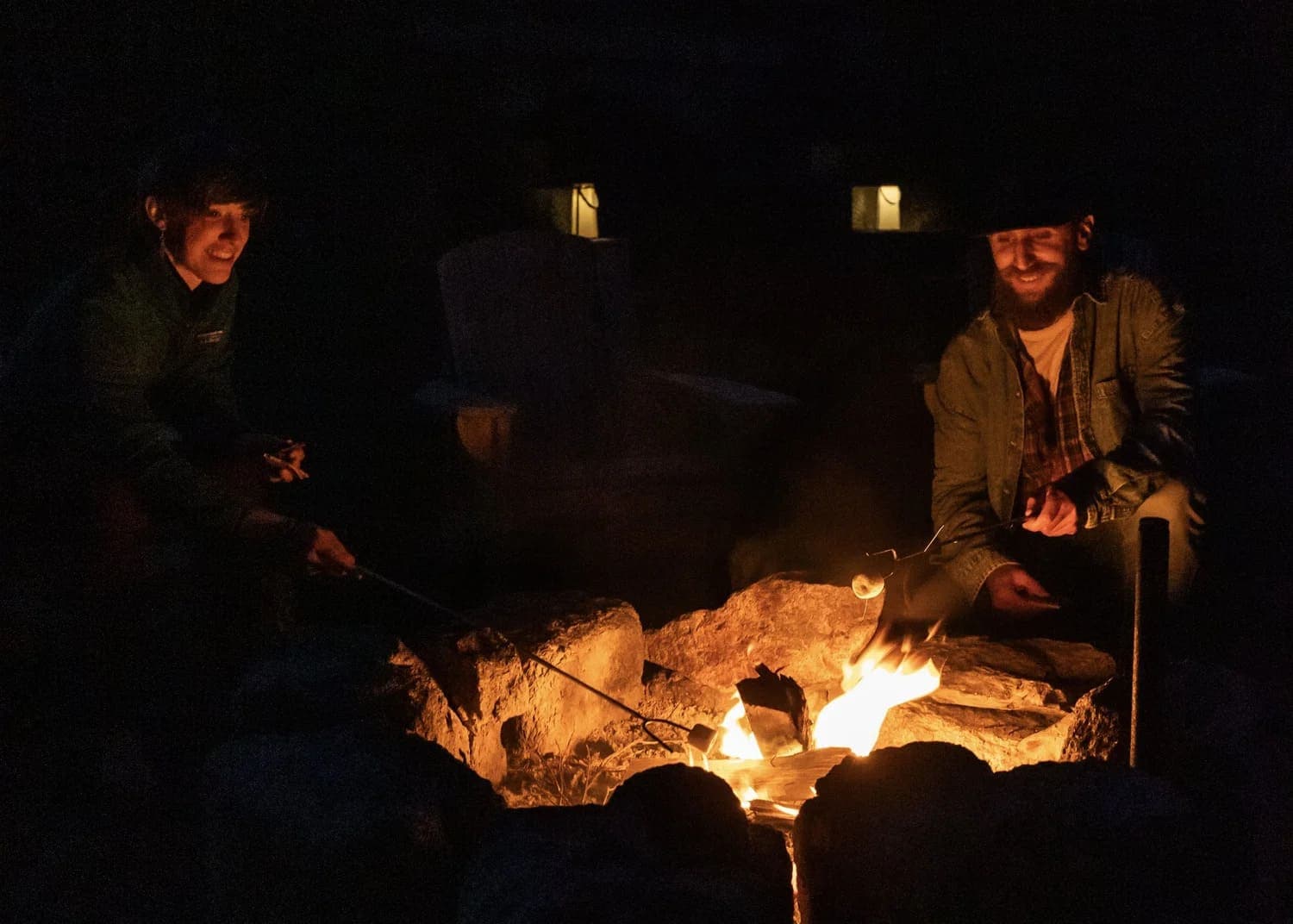 Two people roasting marshmallows over a campfire at night.