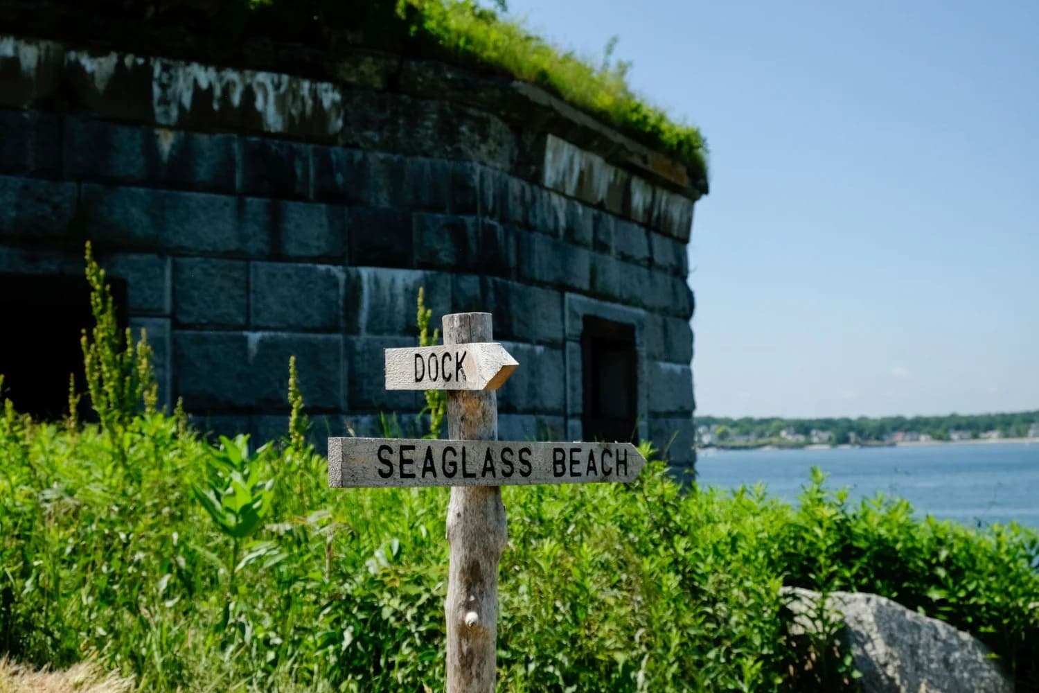A wooden sign points towards "Dock" and "Seaglass Beach" near a stone structure by the water.