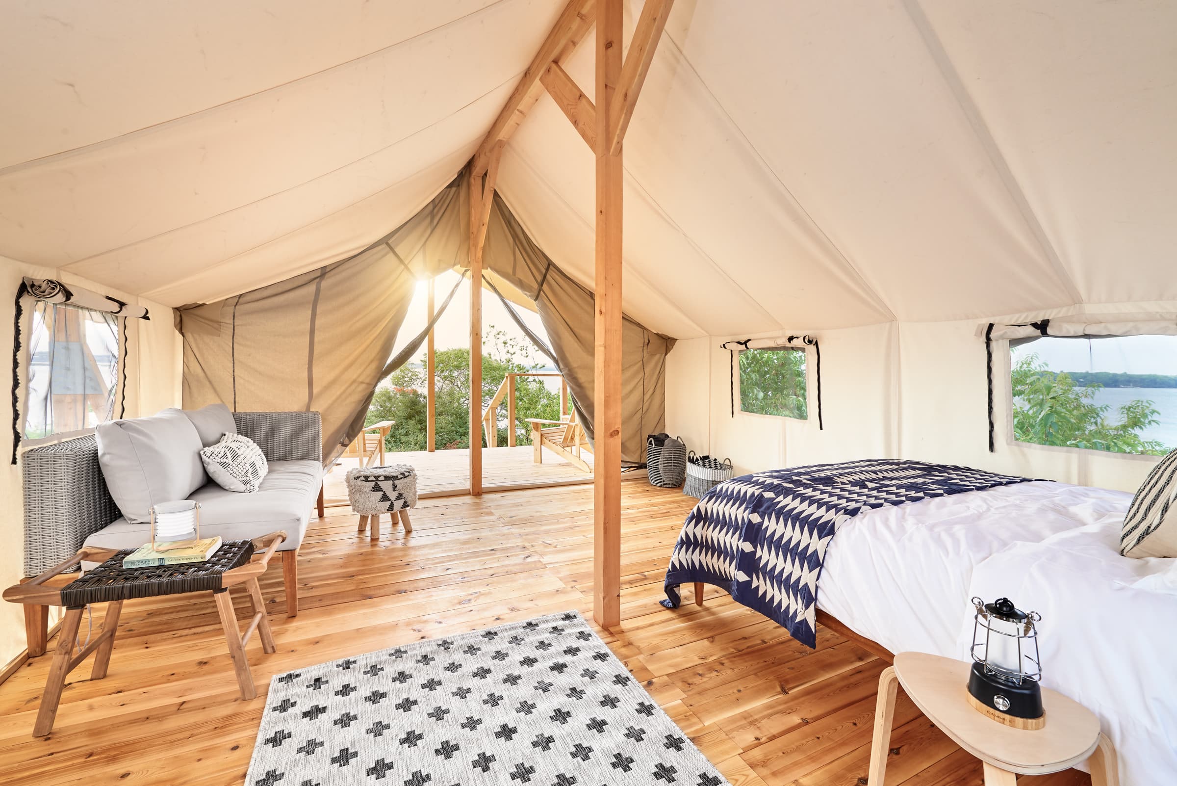 A stylish, tented interior featuring a bed, seating area, and natural light streaming through open flaps.