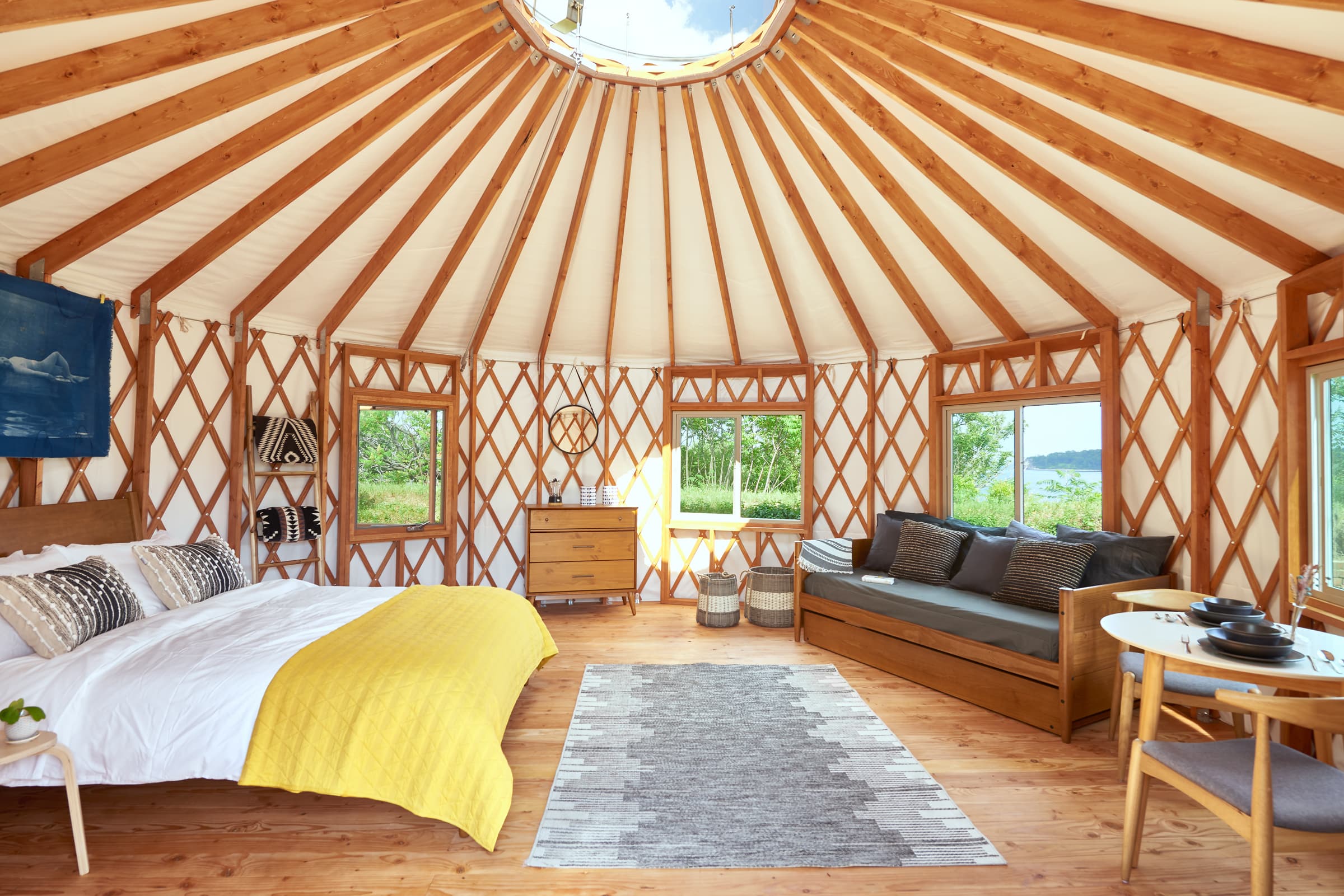 A cozy, circular yurt interior featuring a bed, seating area, and natural light through skylights.