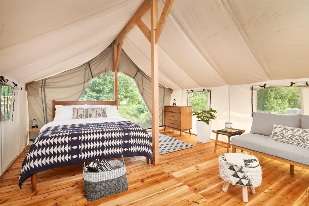 Cozy glamping tent interior featuring a bed, seating area, and wooden flooring.