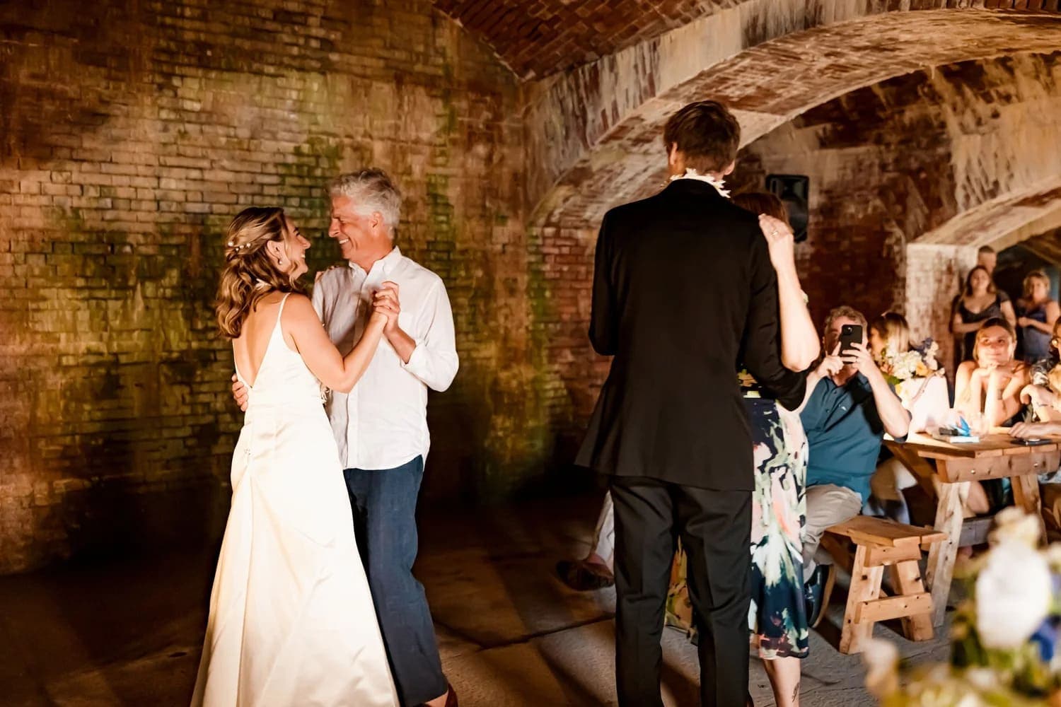 A couple dances together at a wedding reception in a rustic venue while guests watch and enjoy.