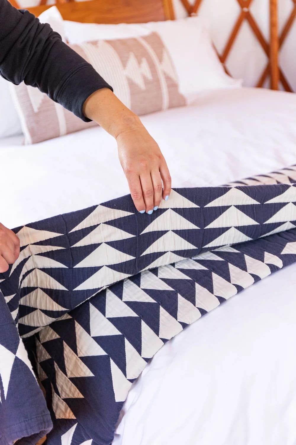 A hand gently adjusts a navy and white patterned quilt on a neatly made bed.