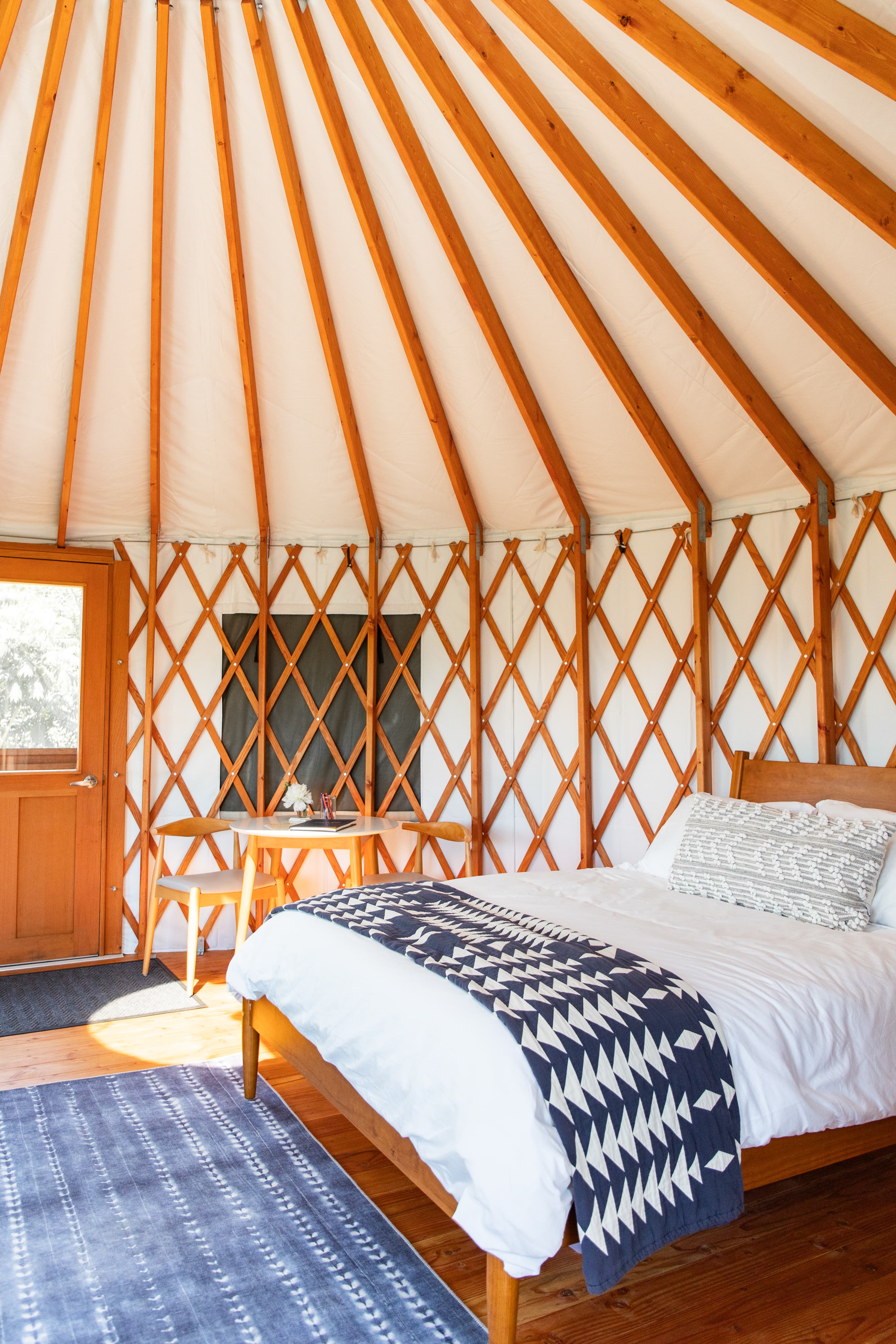 A cozy yurt interior featuring a wooden bed, patterned blanket, and circular wooden beams.