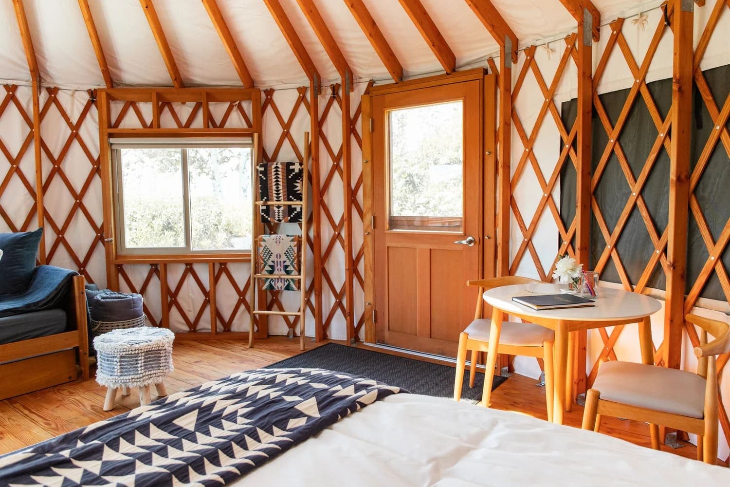 Cozy interior of a yurt featuring wooden beams, a window, and a small dining area.
