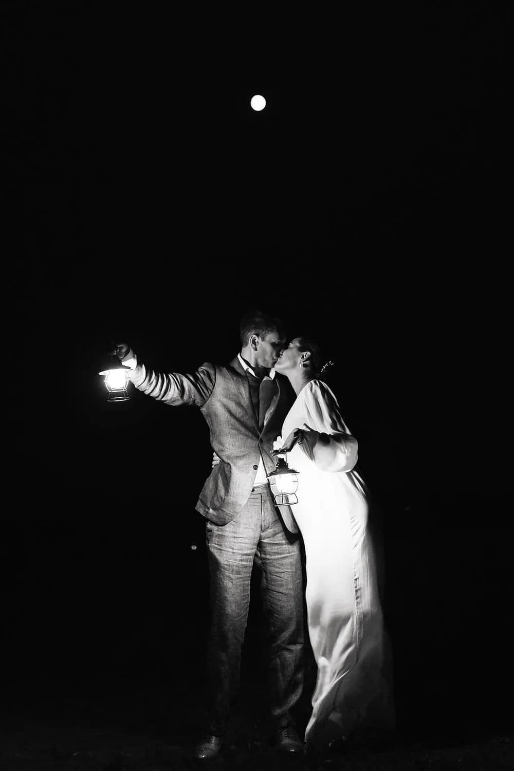 A couple shares a romantic kiss at night, illuminated by a lantern and moonlight.