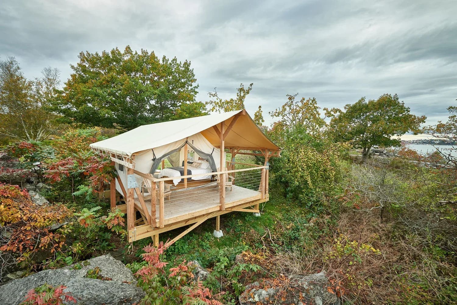 A canvas tent cabin on a wooden deck surrounded by autumn foliage.
