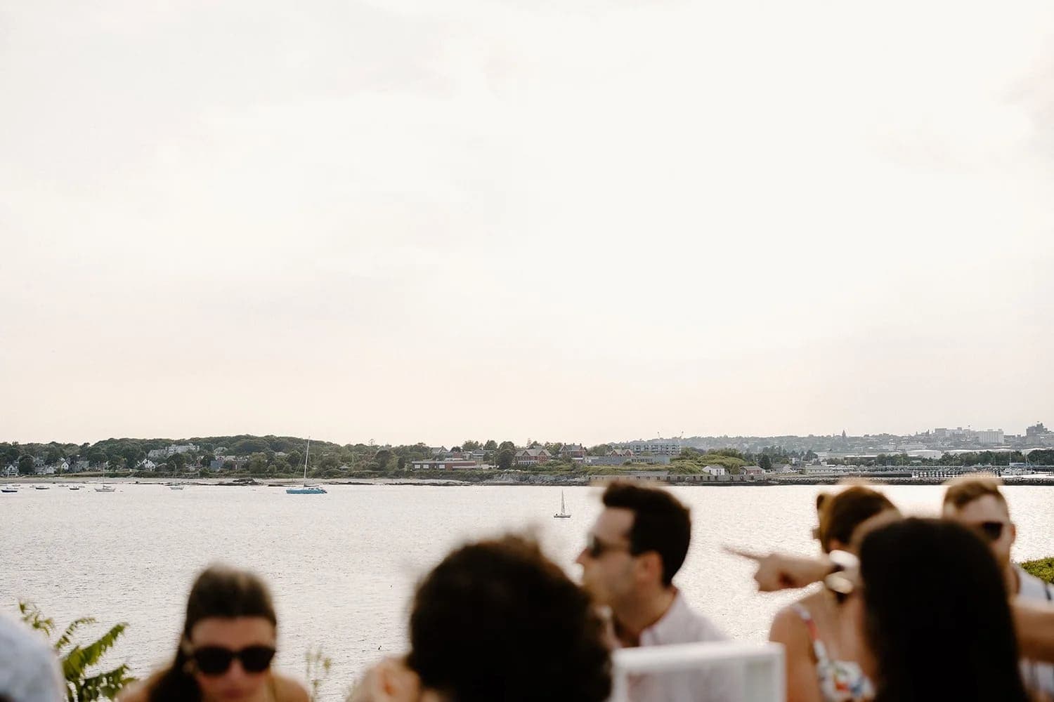 A group of people sit in the foreground with a serene waterfront scene in the background.