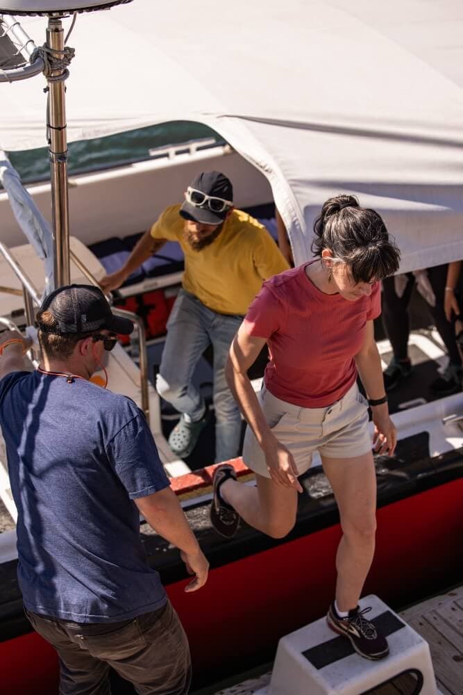 Two peopleboard a boat while another stands nearby on the deck.
