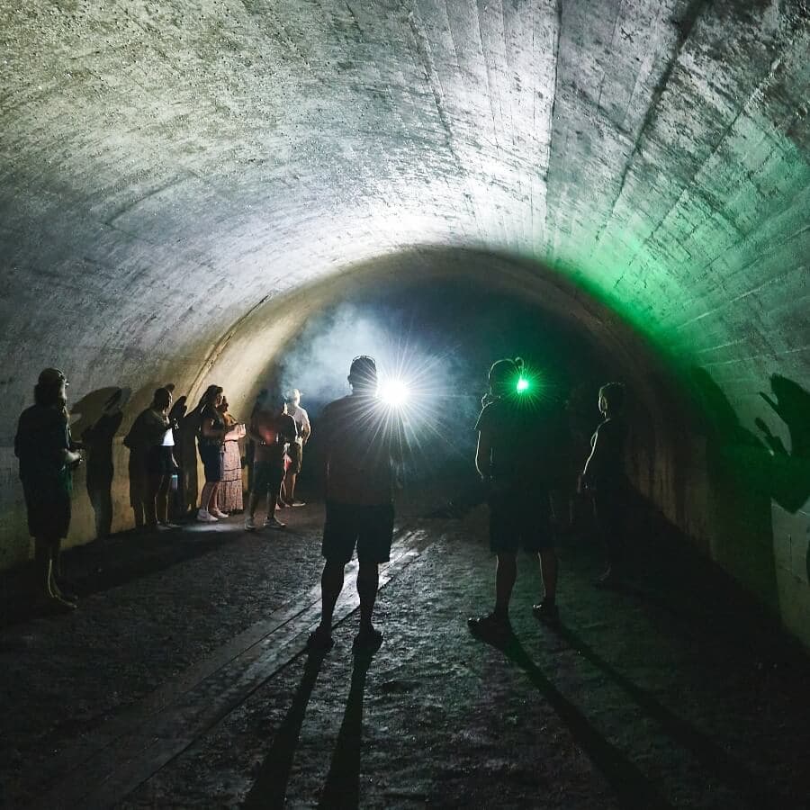 A group of people stands in a dimly lit tunnel, illuminated by bright lights and surrounded by smoke.
